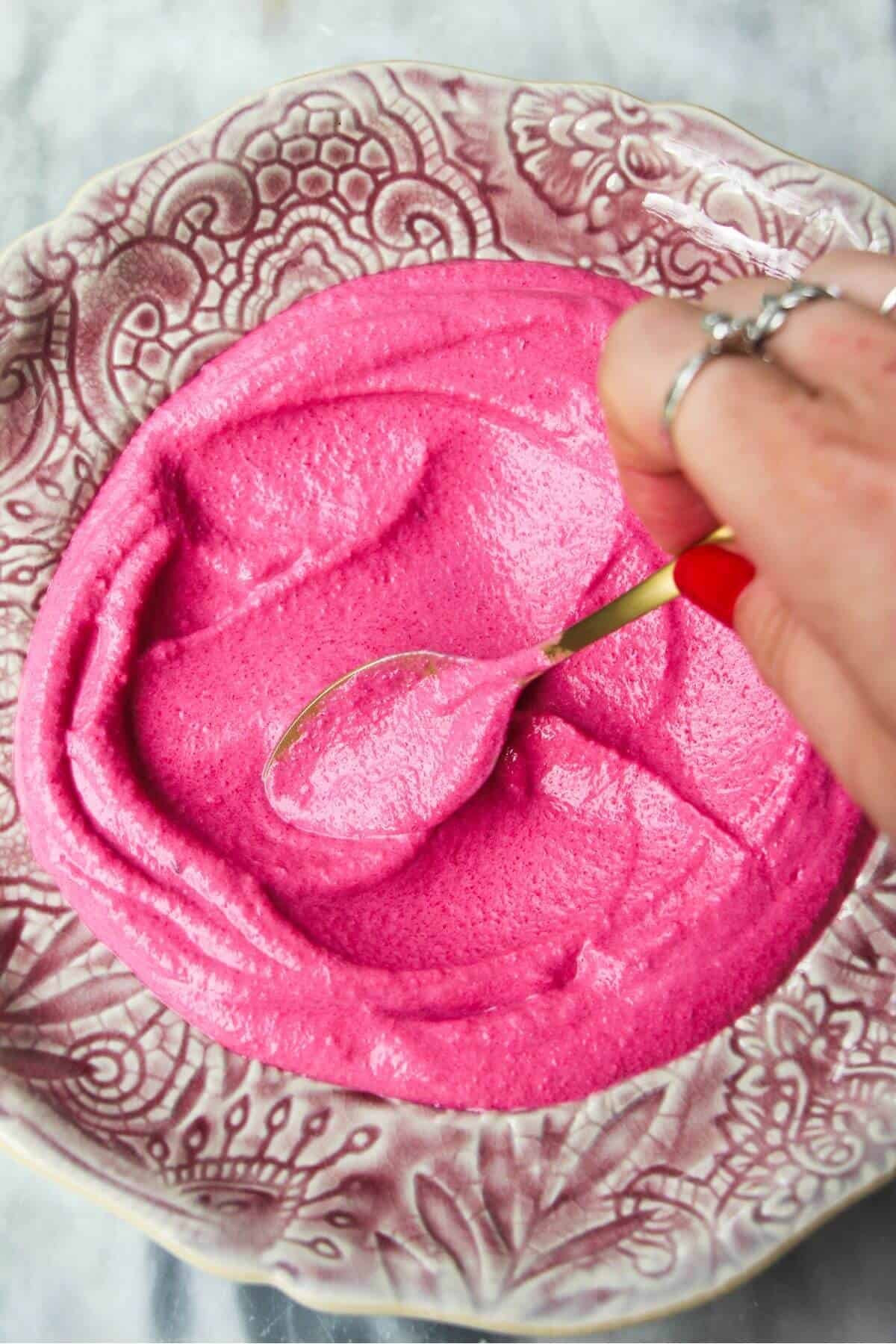 Spooning pink beetroot dip onto a small pink plate.