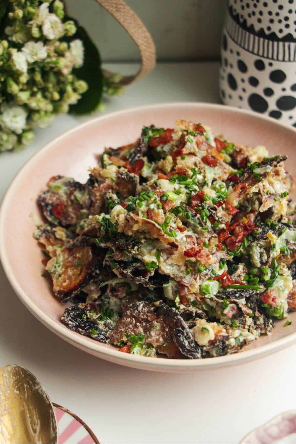 Smashed potato salad in a pink bowl with chives scattered on top.