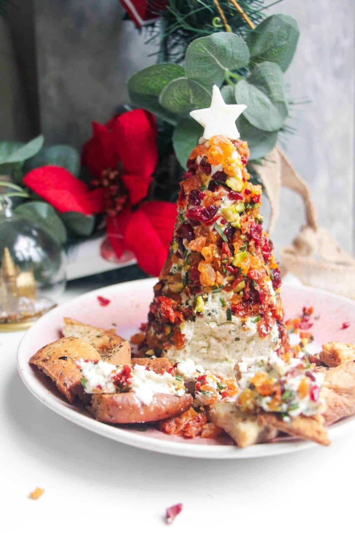 Coated Christmas tree cheese ball topped with a cheese star on a pink plate with pita chips on the side.