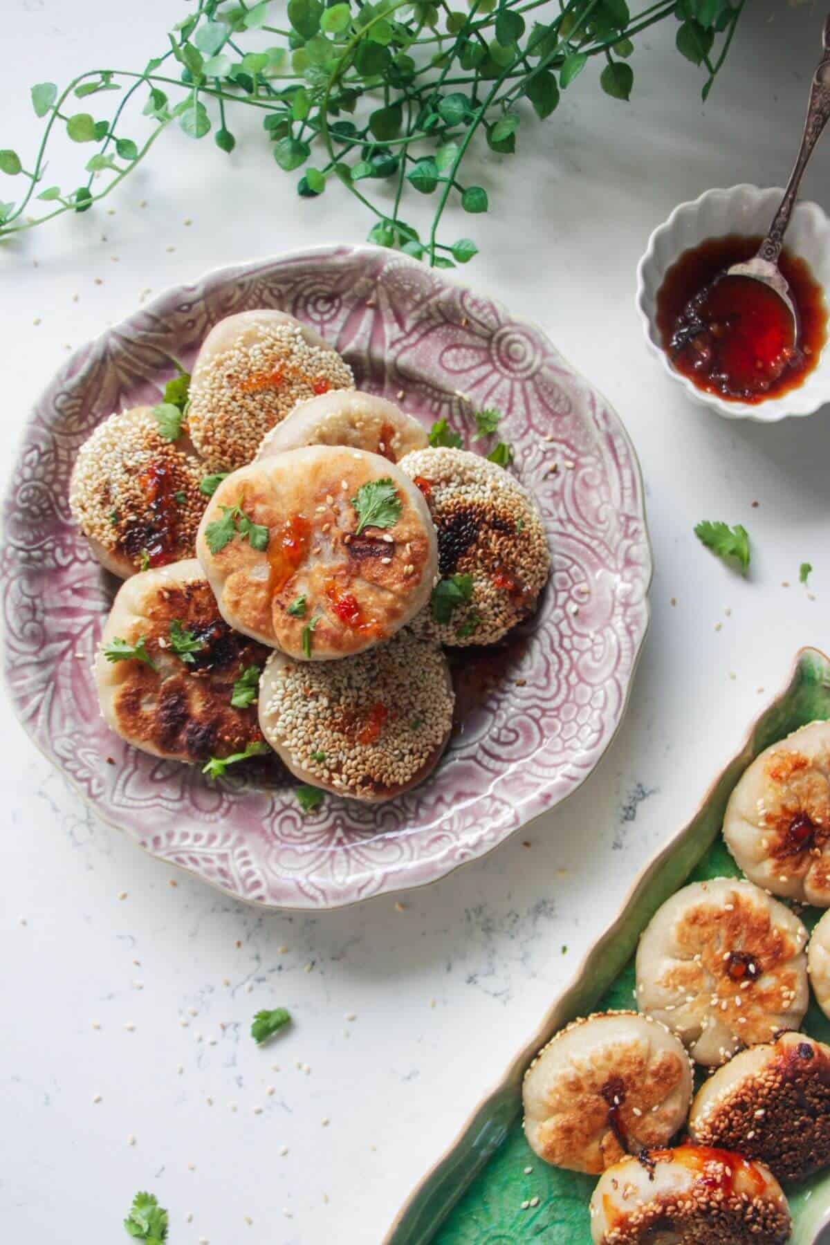Pan-fried gochujang pizza pockets piled on a small pink plate with more pizza pockets on the side on a green plate.
