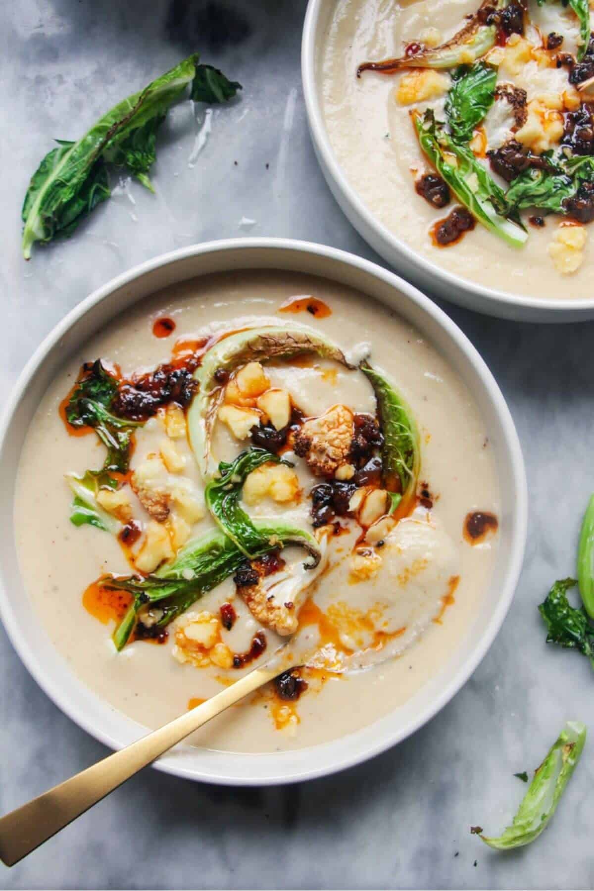 Roasted cauliflower cheese soup in 2 bowls on a grey marble background.