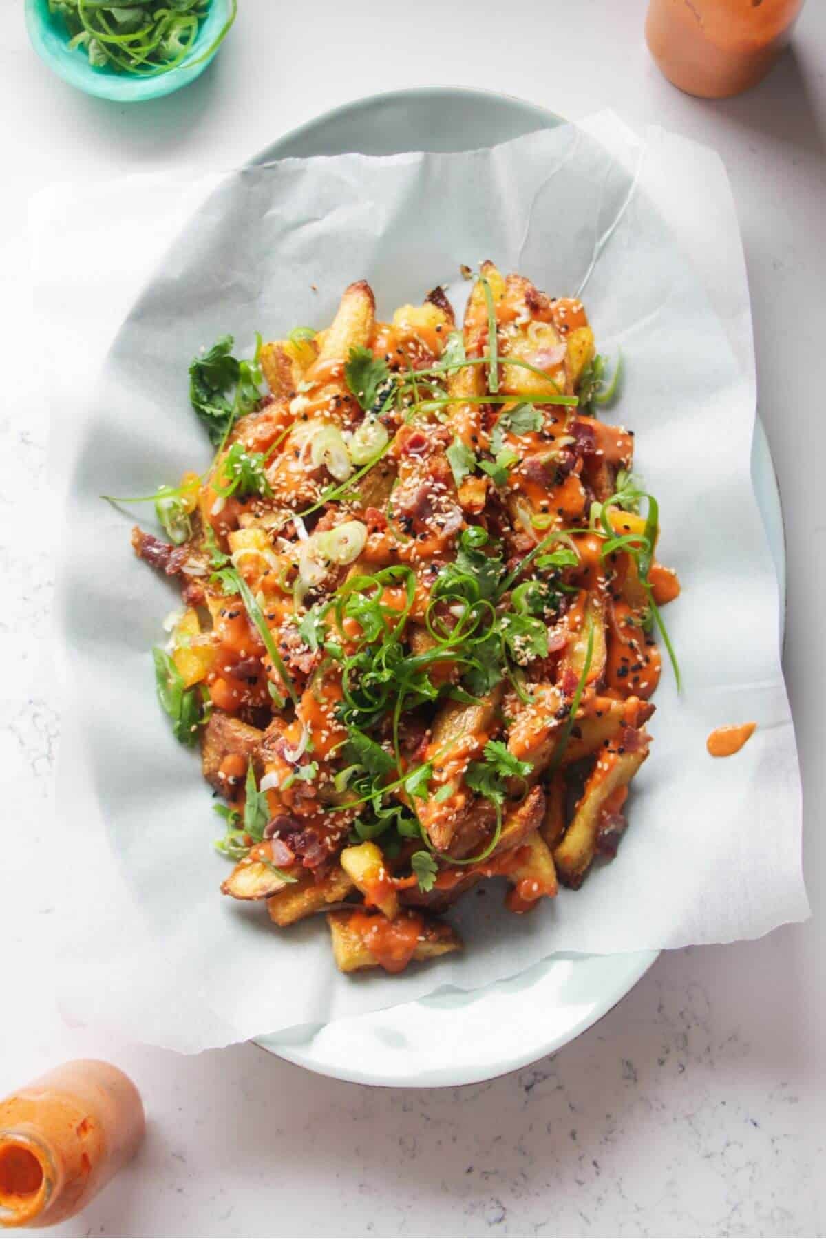 Loaded potato wedges on a large oval white plate with small jug of gochujang bechamel on the side.