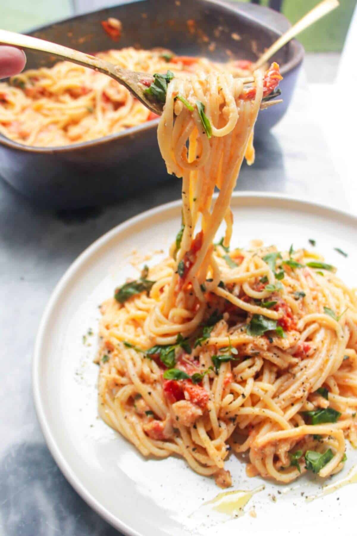 A fork pulling up baked burrata and tomato pasta with dish of pasta in the background.