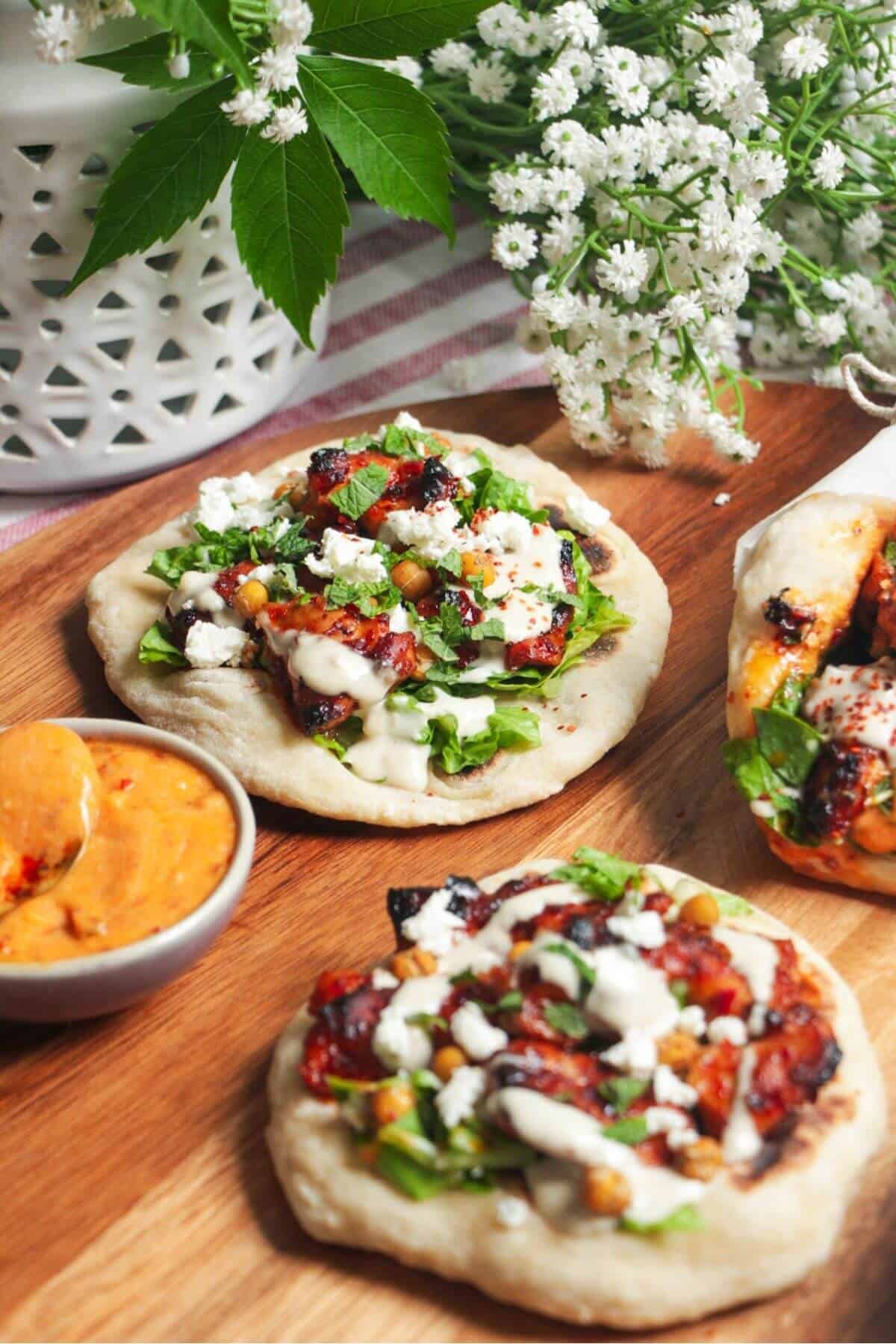 Three flatbreads piled with honey harissa chicken, salad and feta.