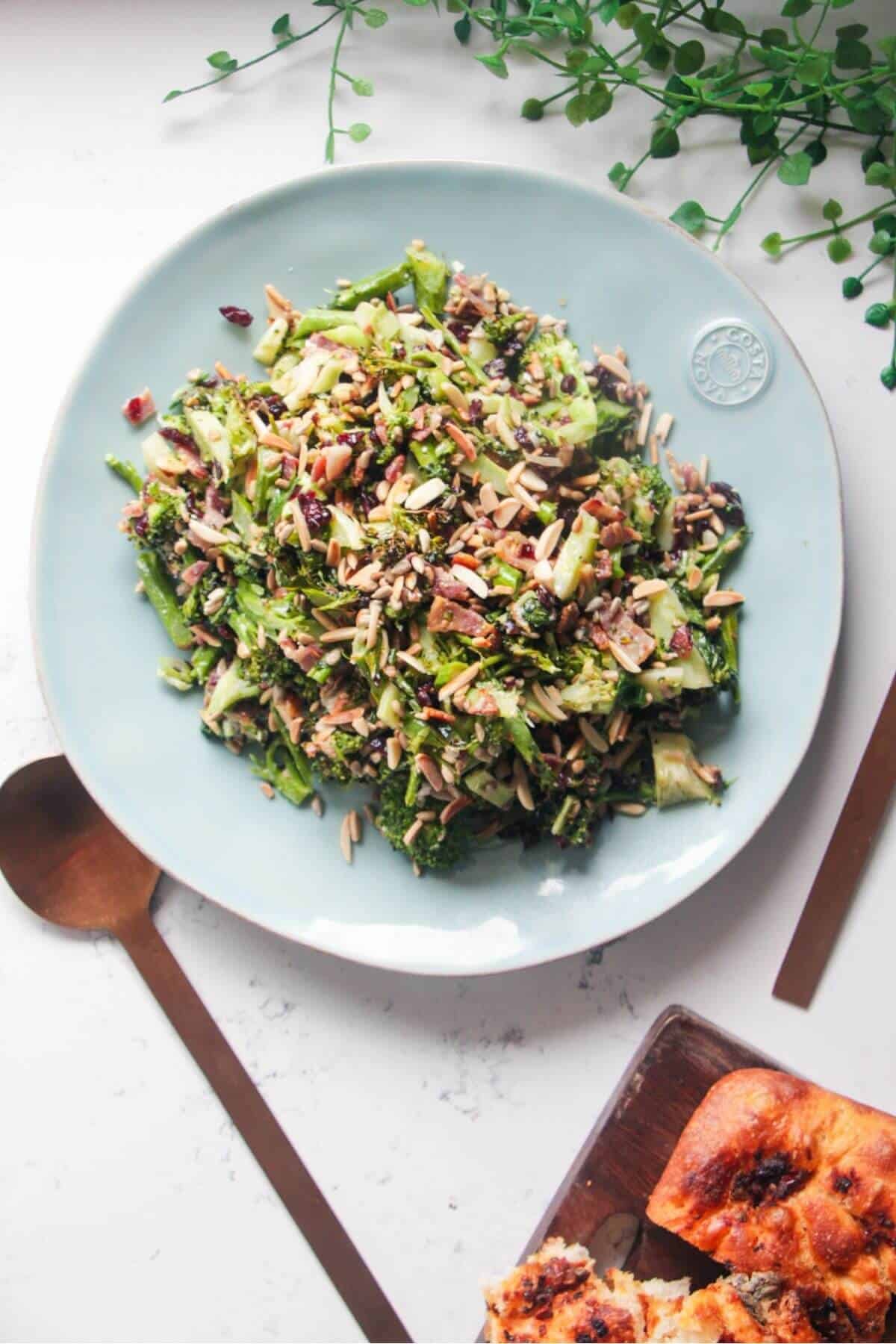 Grilled broccoli crunch salad in a large blue serving plate with focaccia and sunflower seeds on the side.