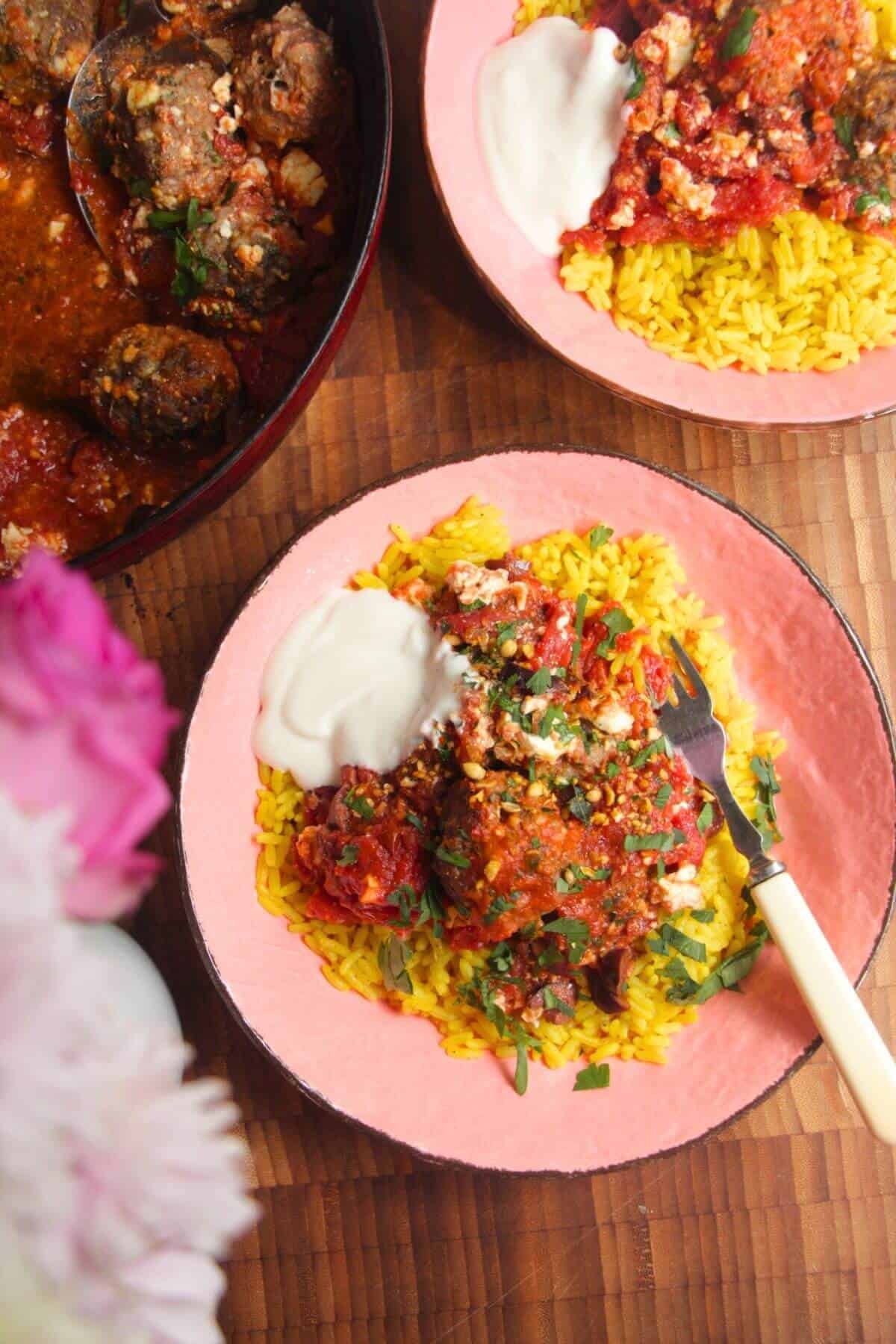 Baked meatballs in tomato sauce on top of golden rice in a pink bowl.