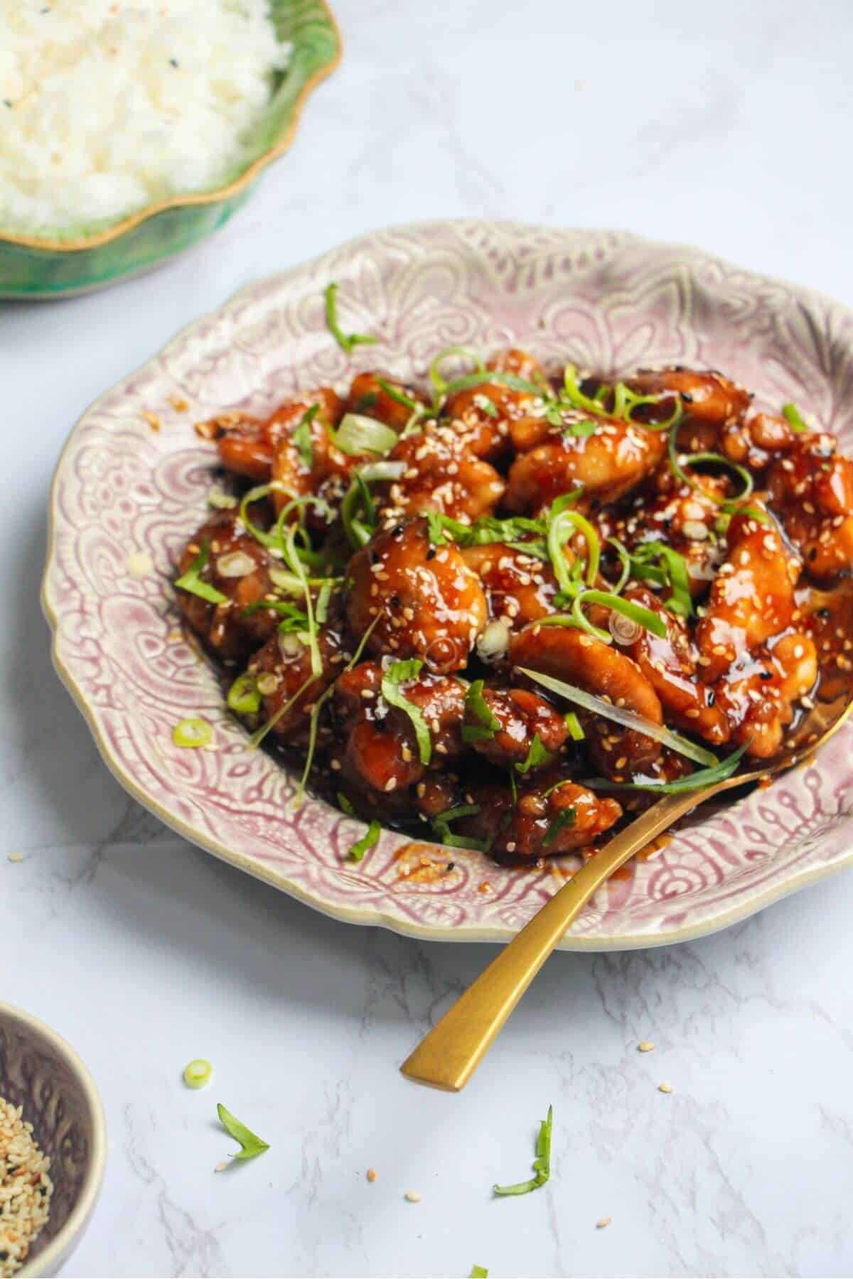 Honey sesame chicken topped with cilantro and scallions on a pink plate.