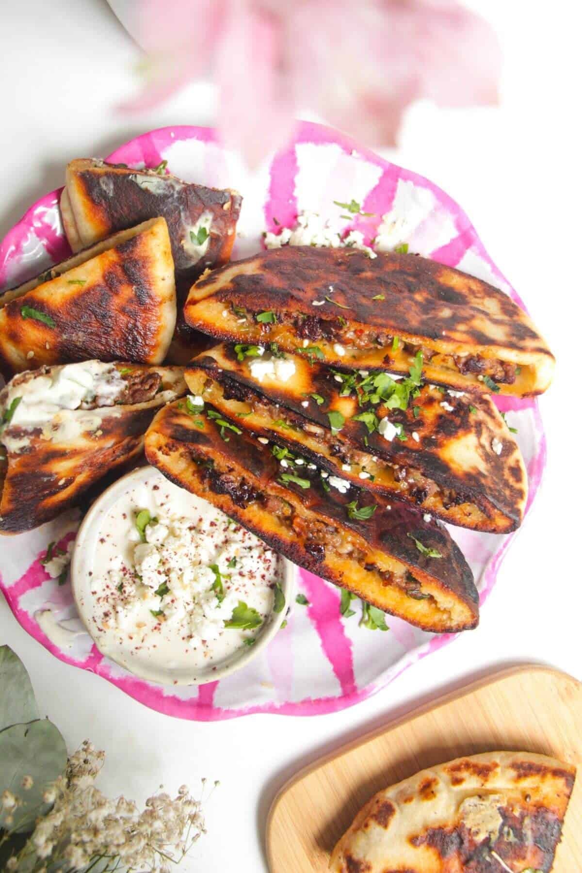 Three stuffed flatbreads on a pink and white plate with tahini sauce on the side.