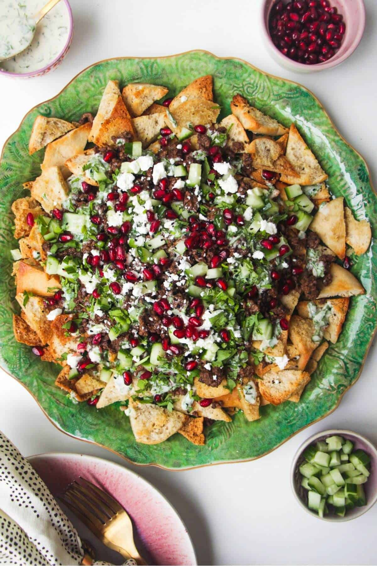 Middle Eastern style nachos on a green plate, with cucumber on the side.