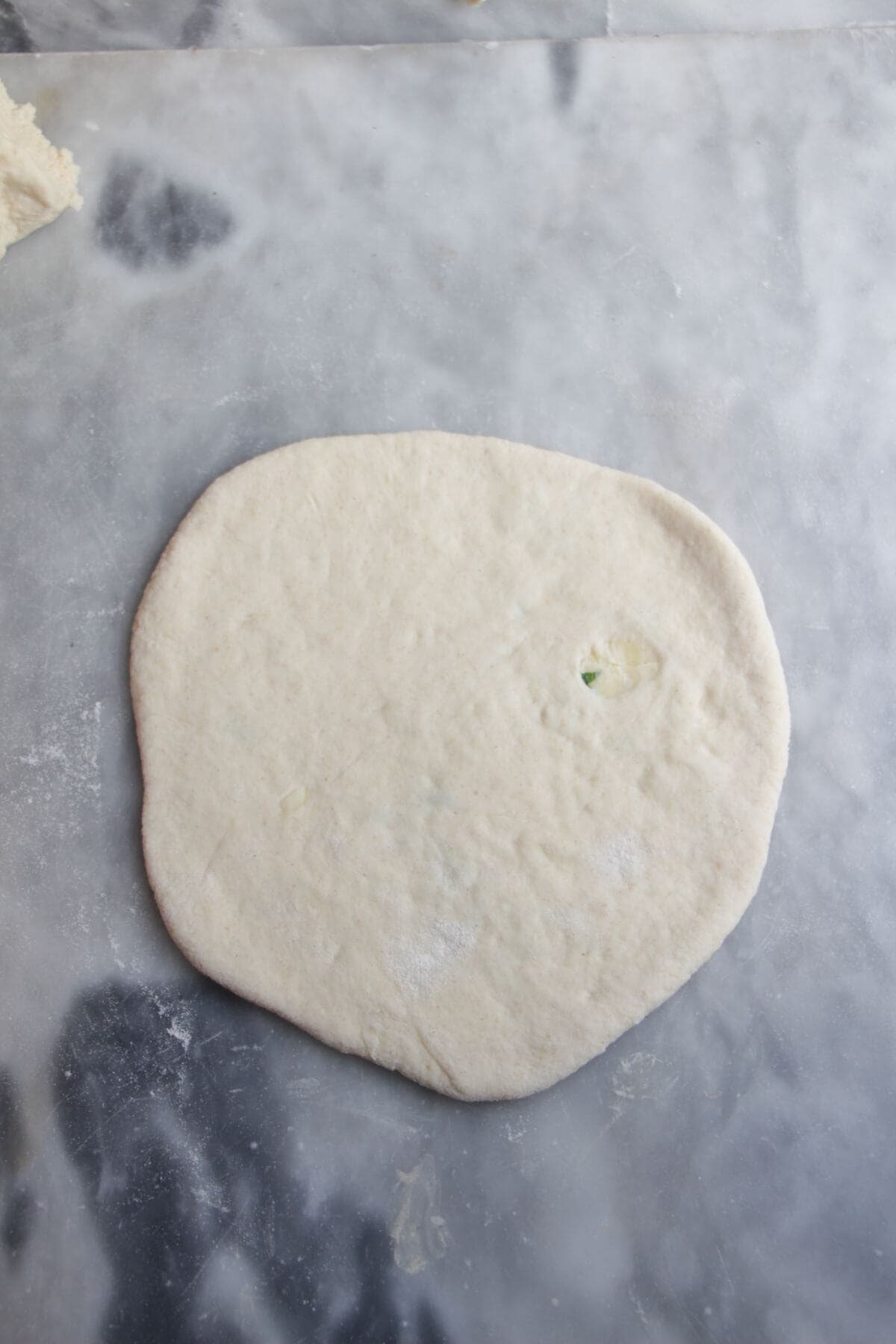 Rolled out cheese stuffed naan on a grey marble background.