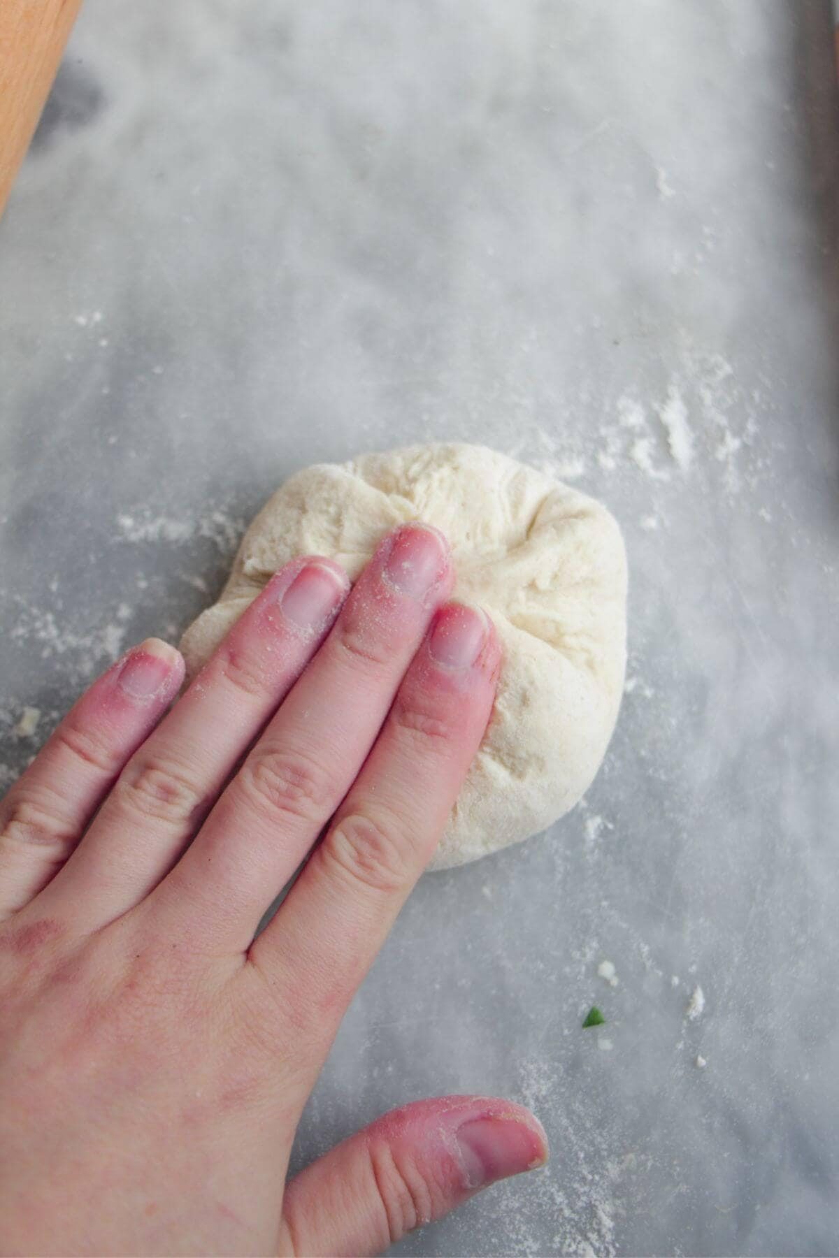 Hand pressing down to seal cheese into naan dough.