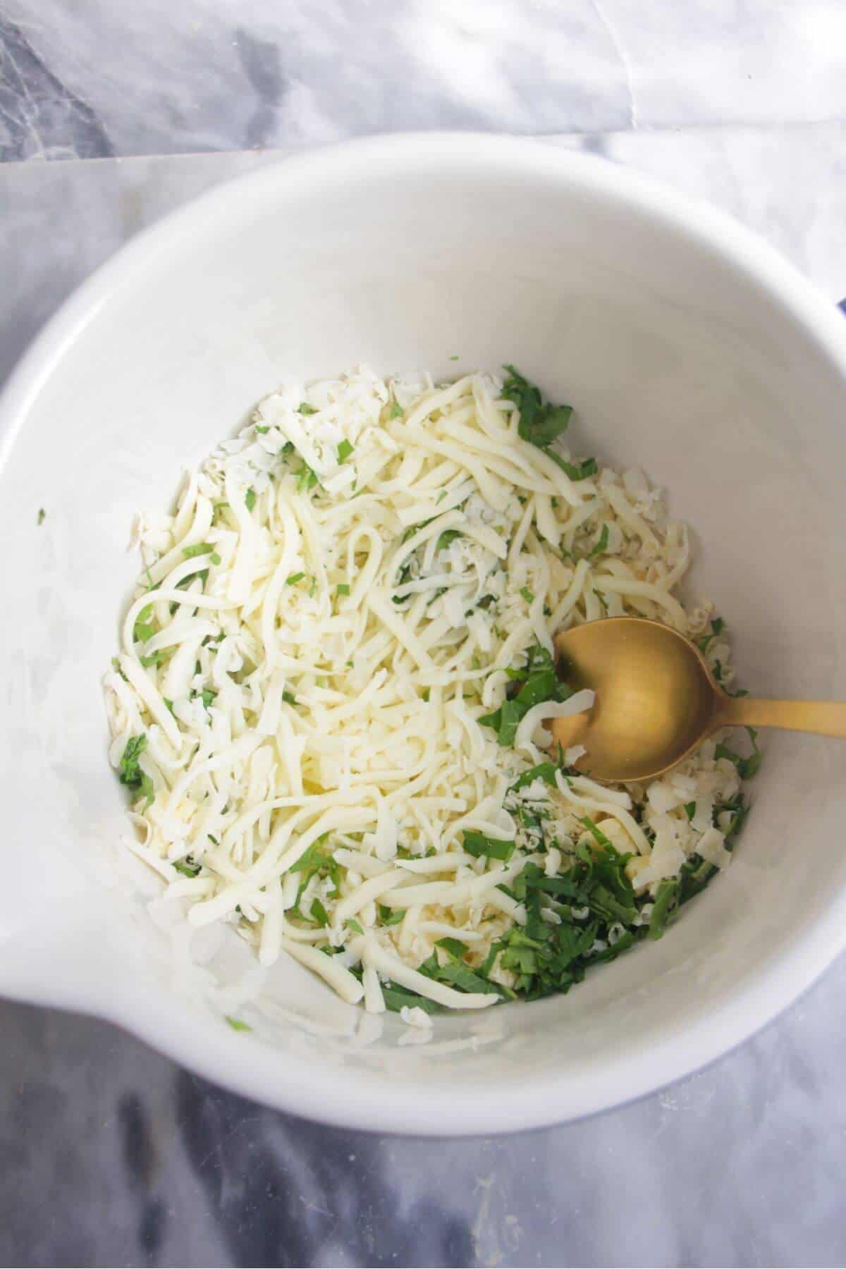Grated cheese and chopped green herbs being mixed in a small white bowl.