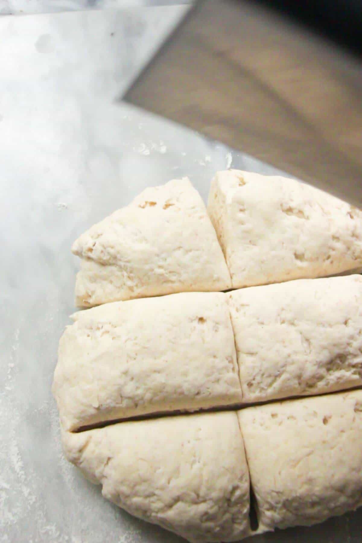 Dough being divided in 6 with a silver dough scraper on a grey marble background.