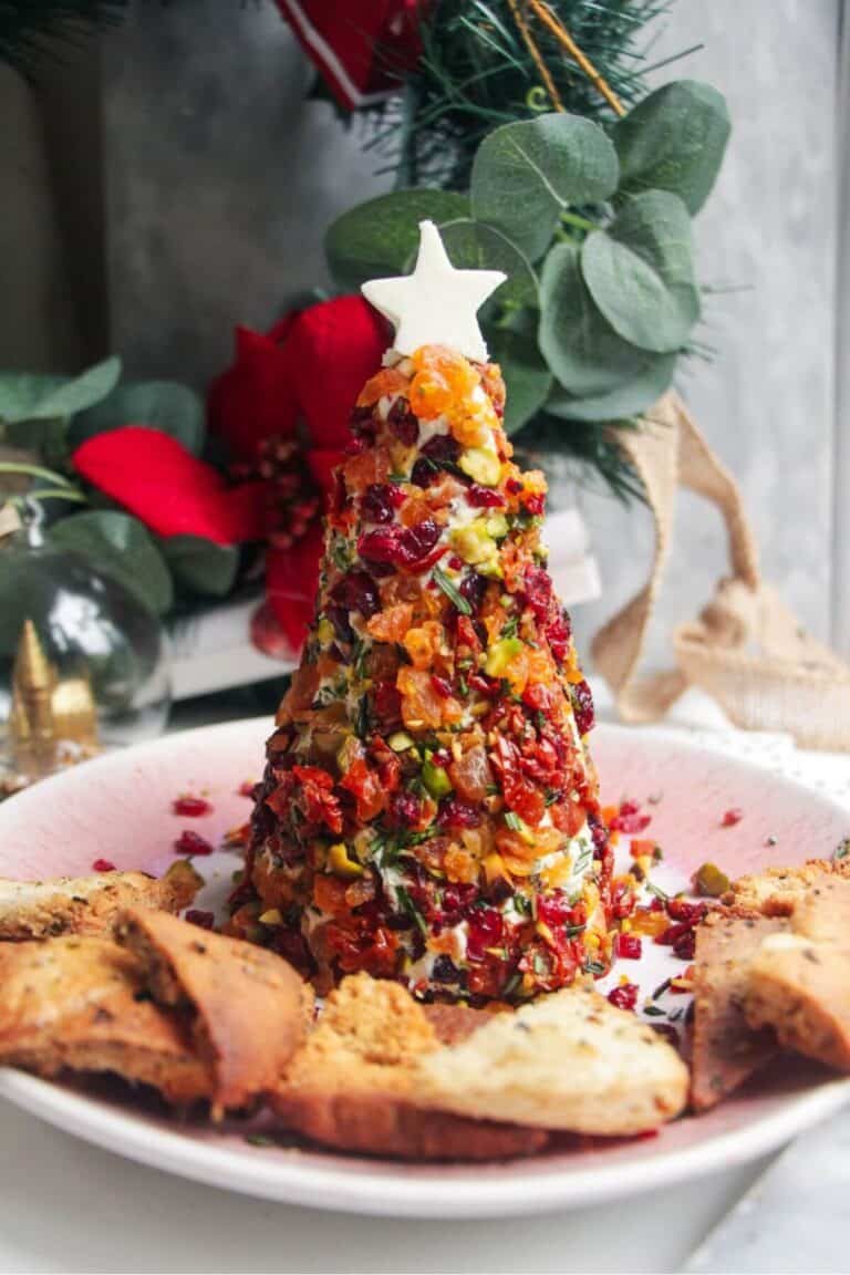 Coated Christmas tree cheese ball topped with a cheese star on a pink plate with pita chips on the side.