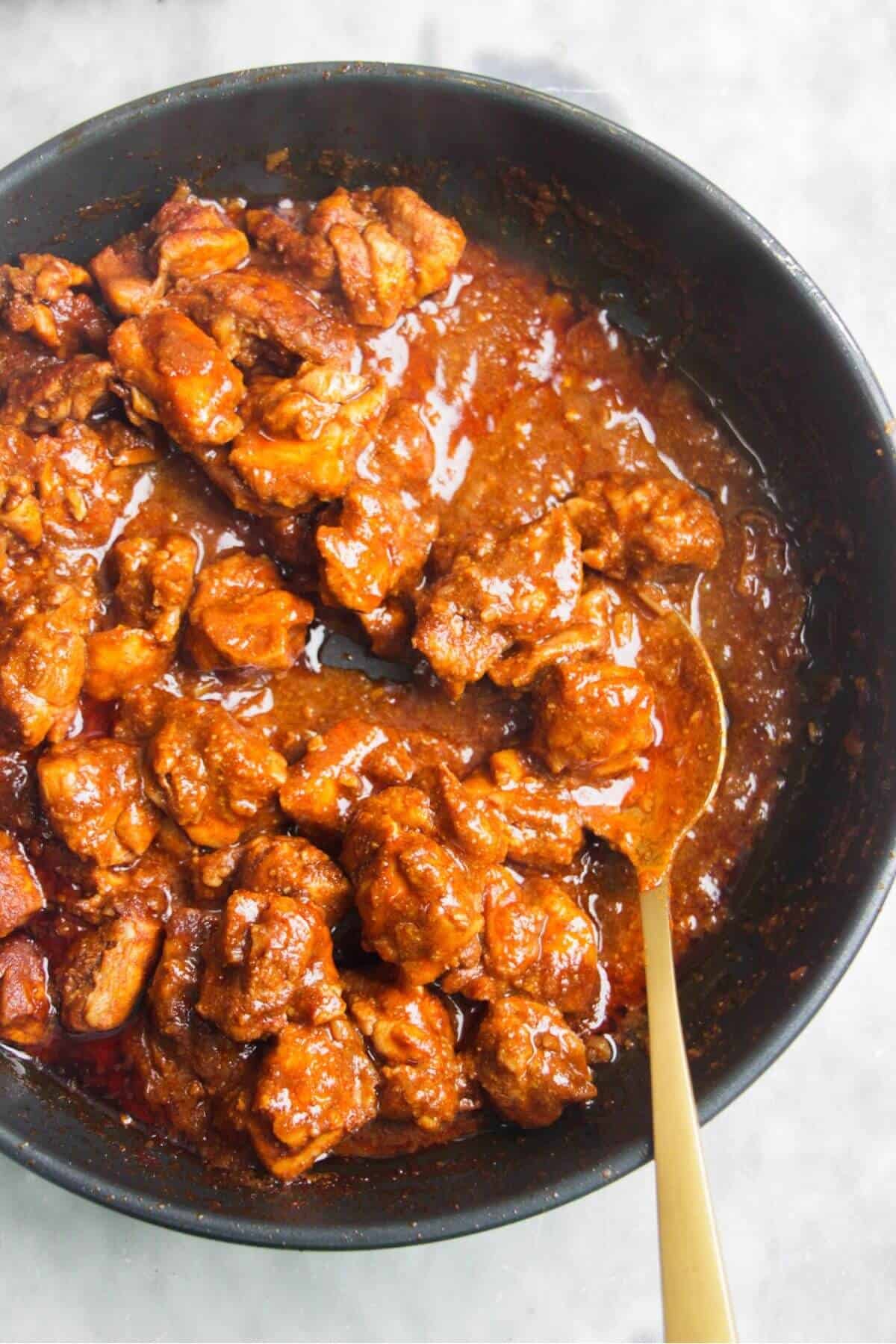 Thickened chicken rogan josh in a small frying pan with a gold spoon inside.