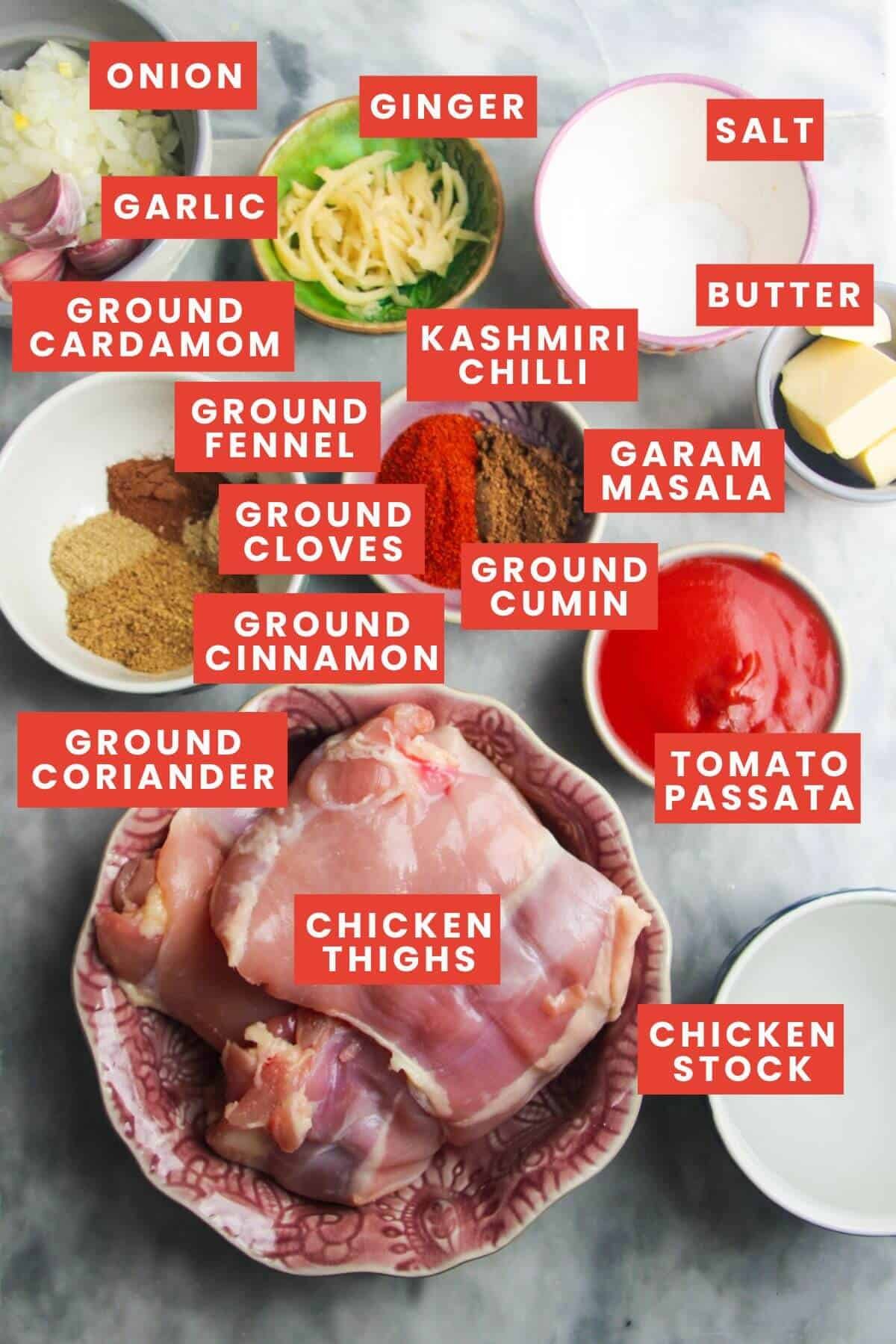 Ingredients for chicken rogan josh laid out on a grey marble background and labelled.