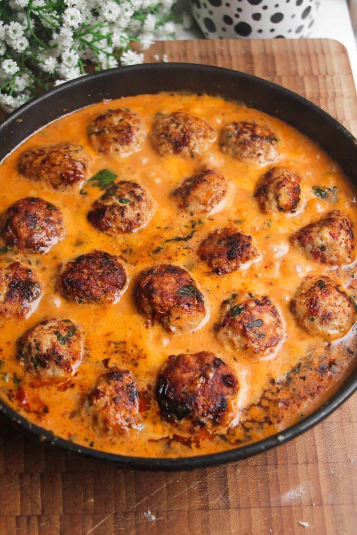 Browned meatballs simmering in 'Marry Me' sauce in a pan.