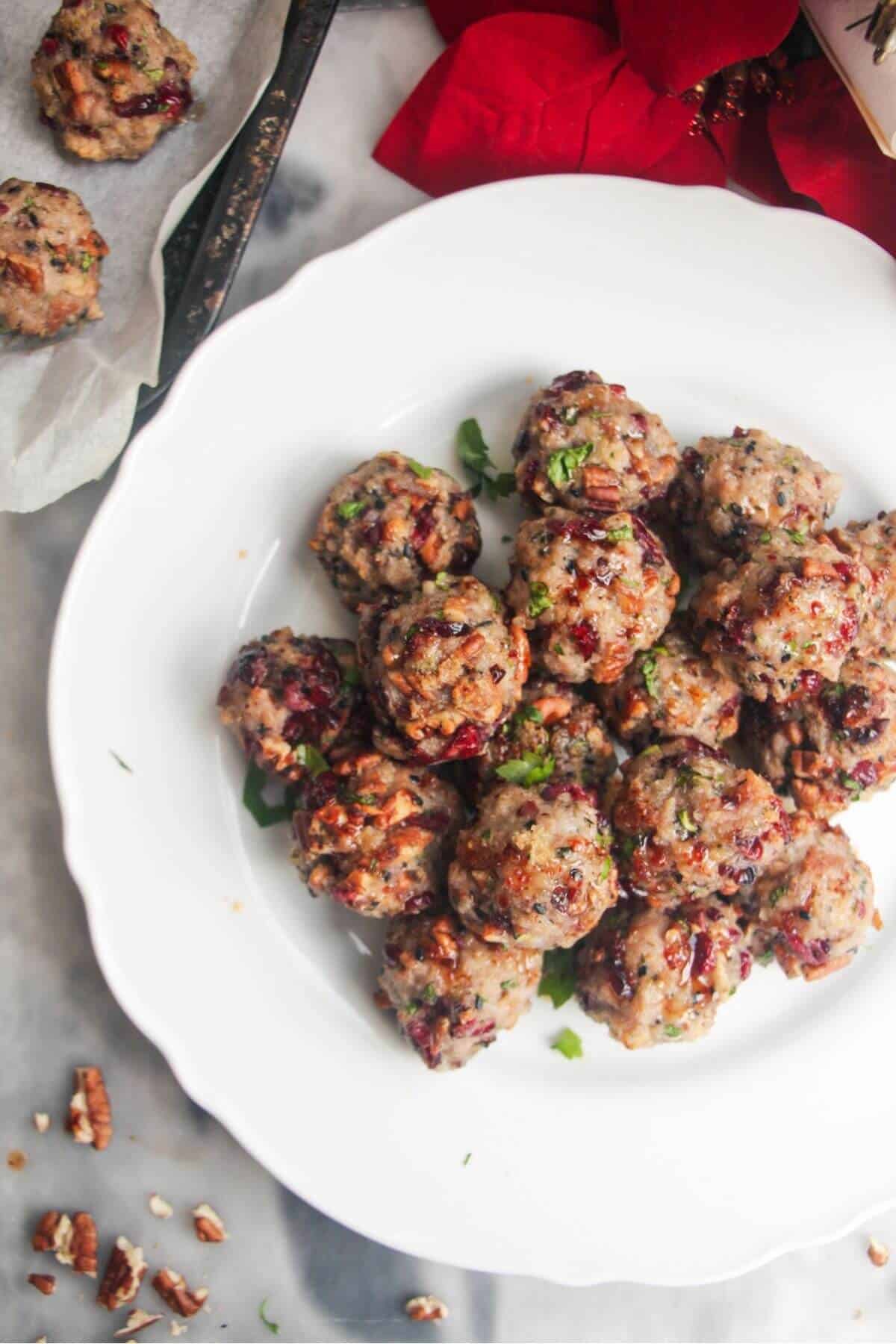 Cranberry pecan stuffing balls piled on a large white plate with more stuffing balls in the background.