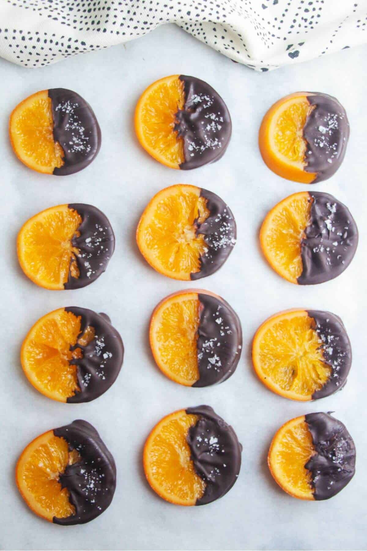 Dark chocolate dipped candied orange slices laid out on a baking paper lined tray.