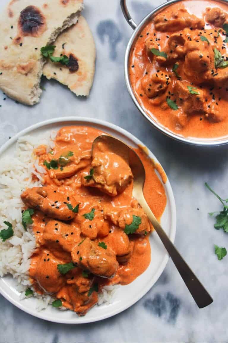 White plate with rice and butter chicken with bowl of butter chicken in the background and garlic naan.