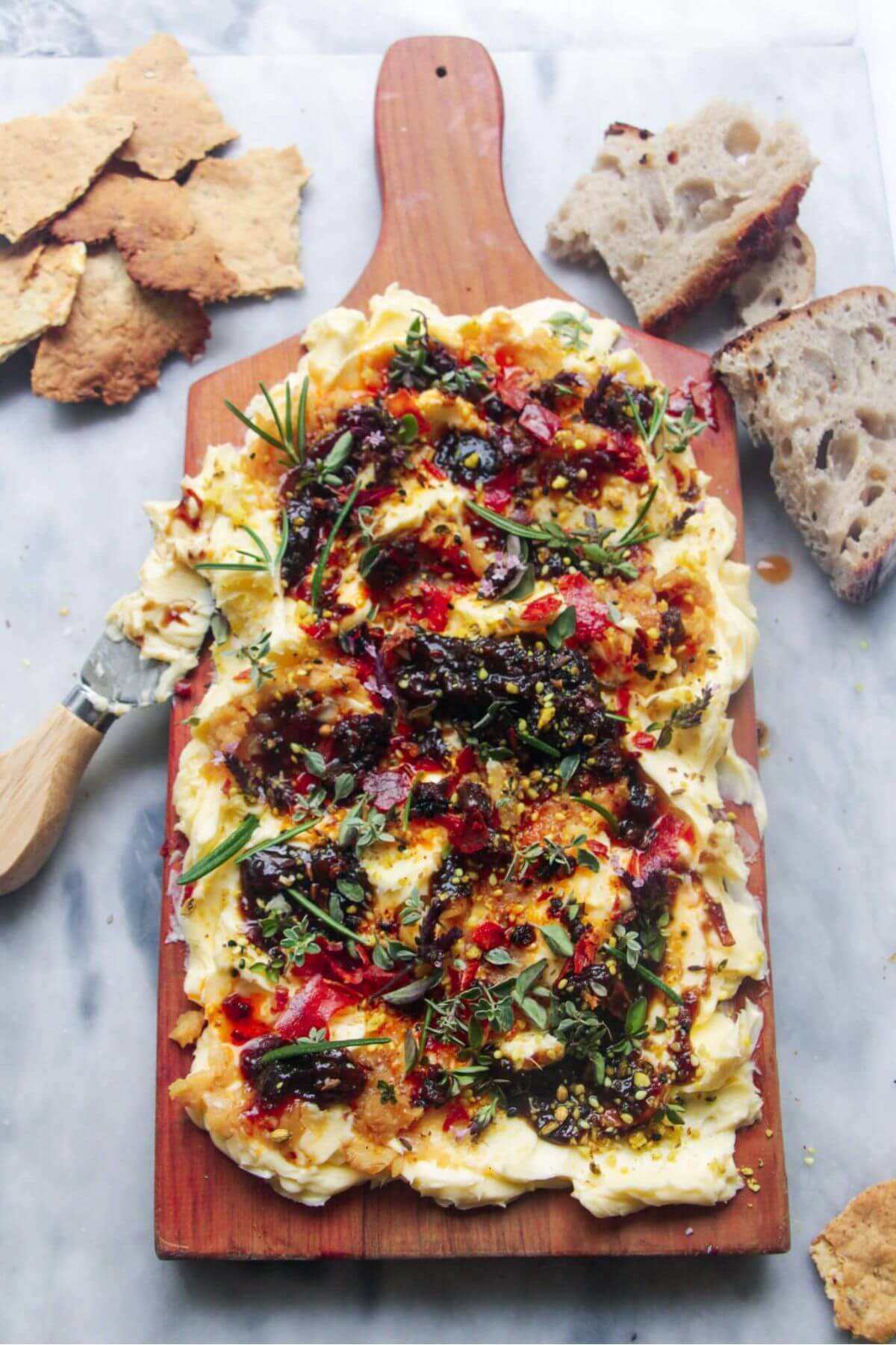 Butter smoothed onto a board and topped with chilli oil, fig chutney and herbs with crackers and bread on the side.
