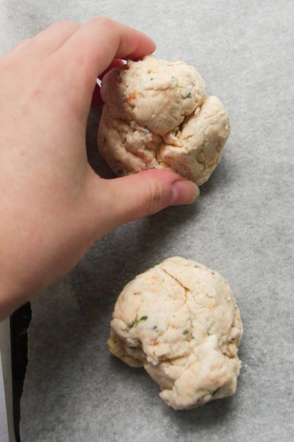 Hand placing cheese scones on a lined baking tray ready to be baked.