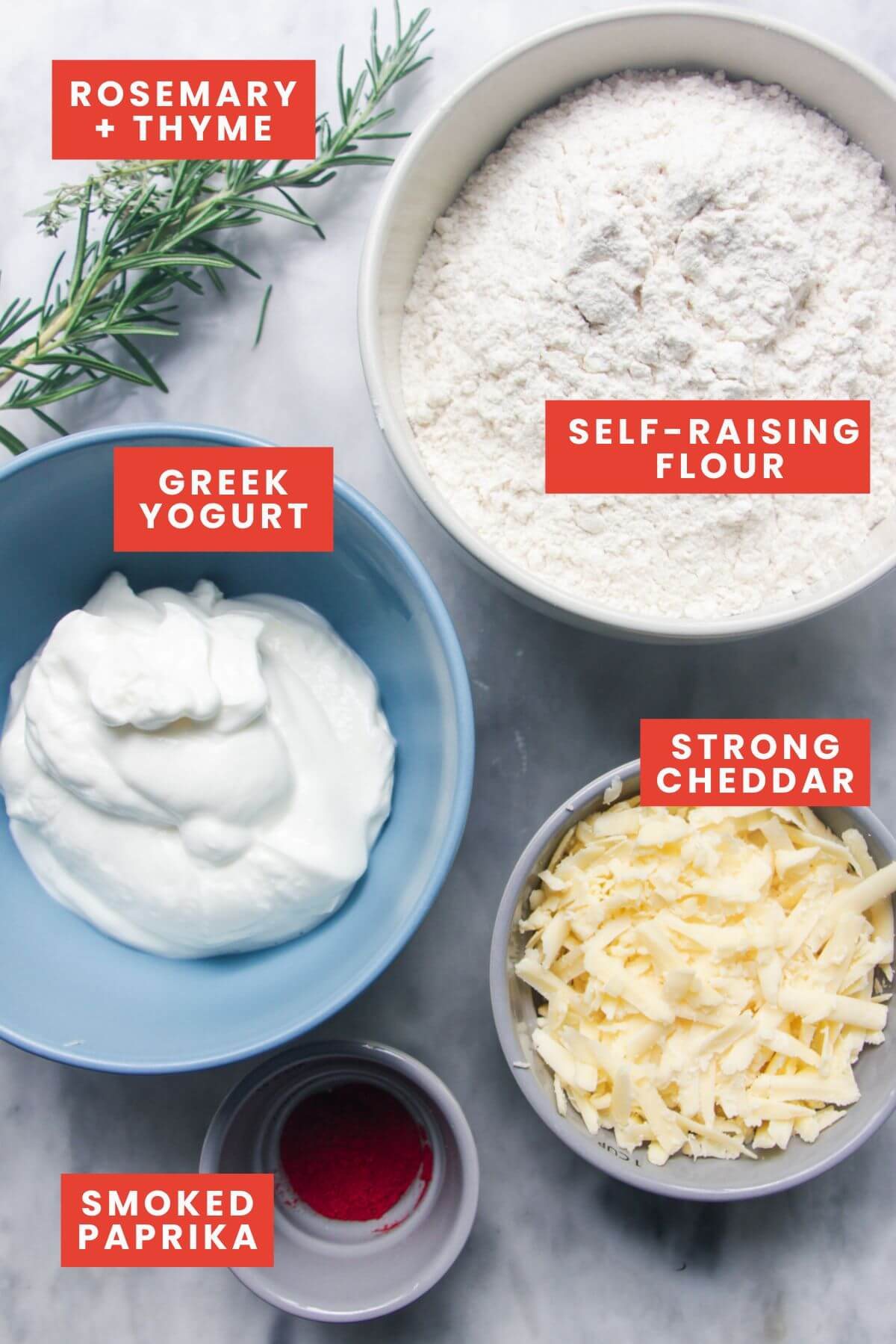 Herby cheese scone ingredients laid out on marble background and labelled.
