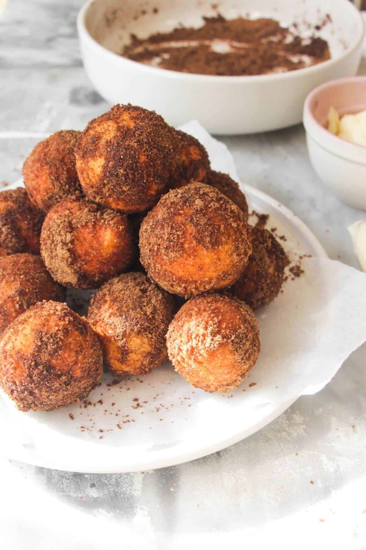 A pile of sugar coated donut bites on a small white plate, with bowl of more pumpkin spice sugar in the background.