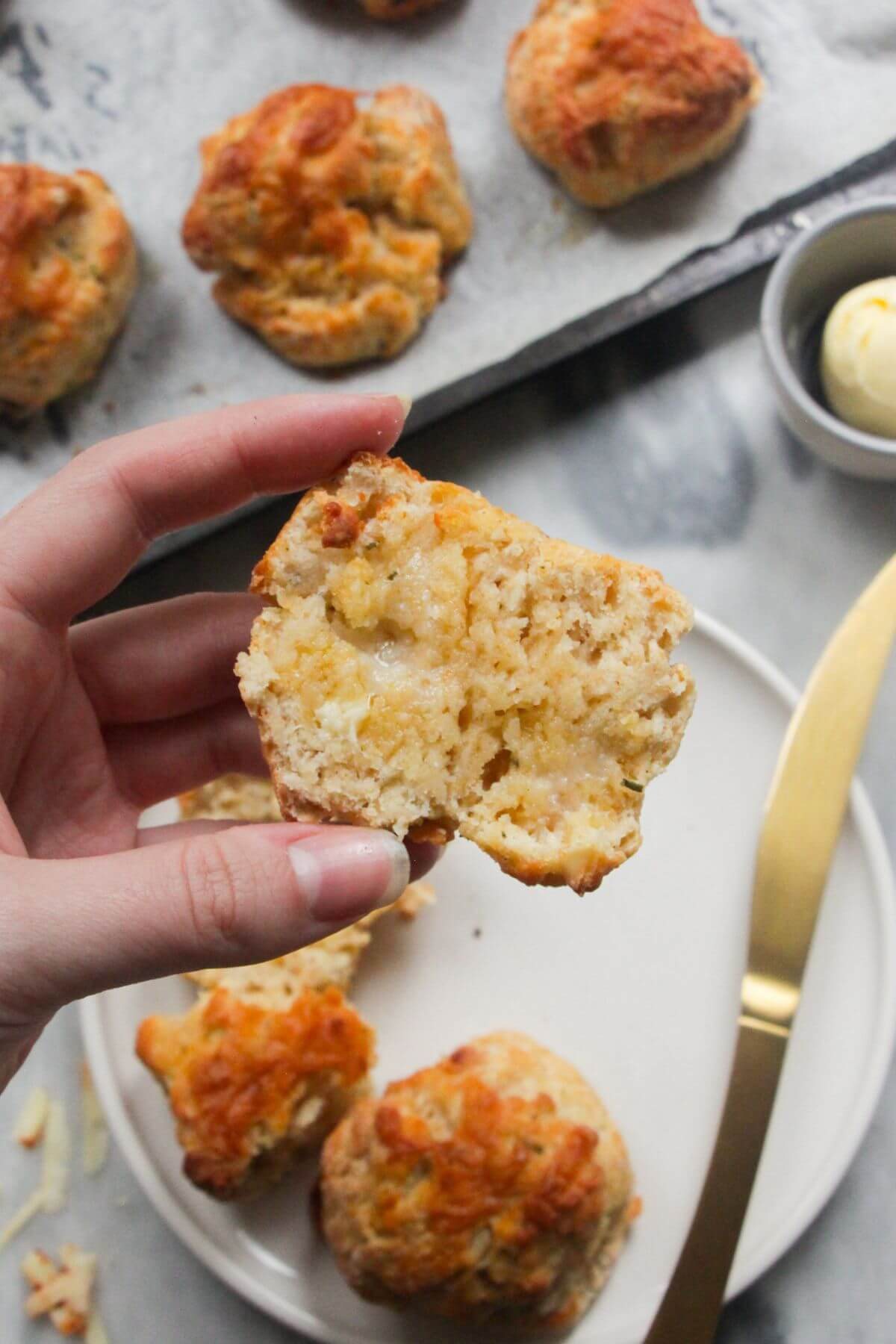 Hand holding up a sliced in half cheese scone with more cheese scones in the background.