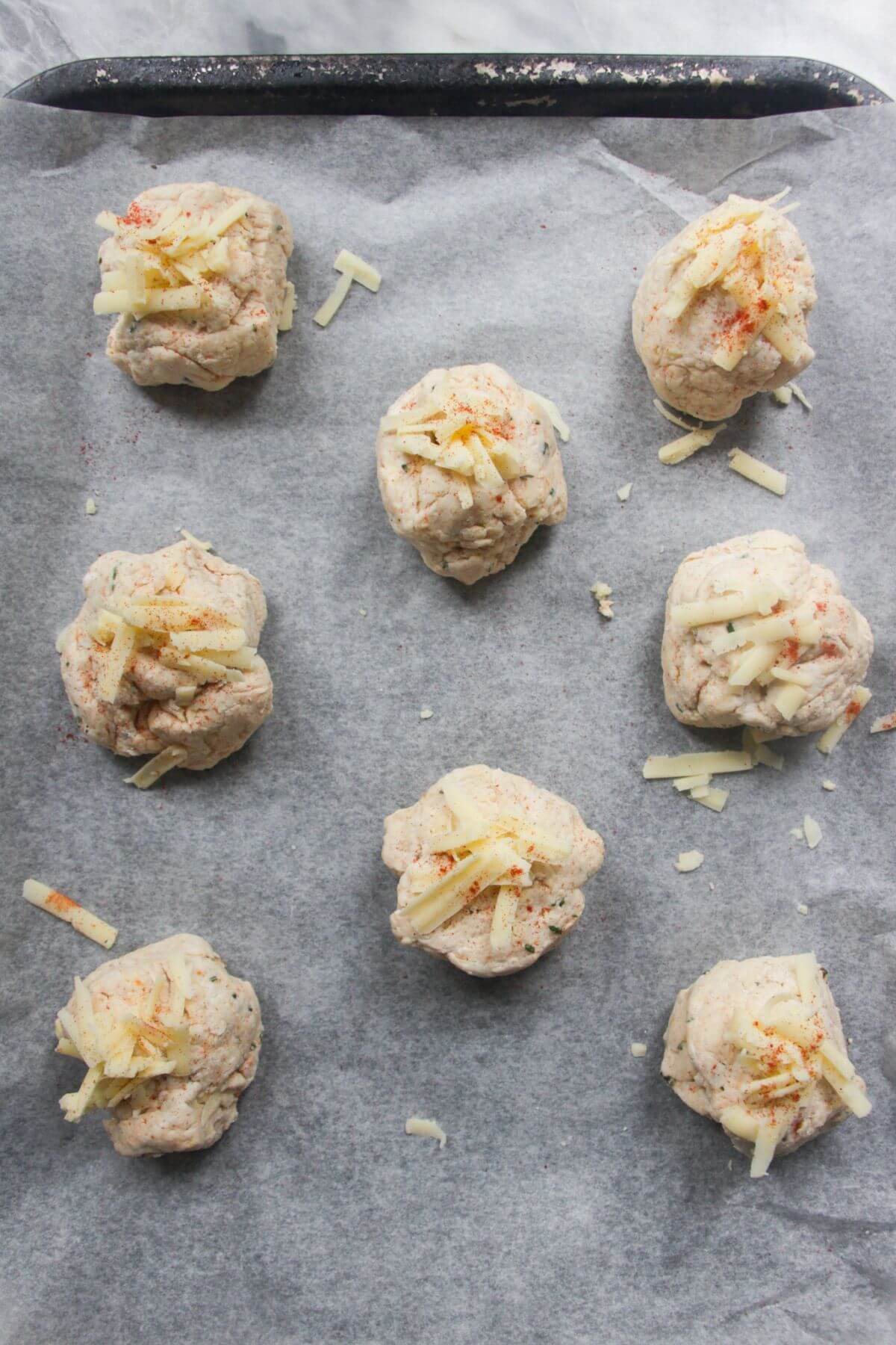 8 cheese scones laid out on a baking paper lined oven tray ready to be baked.