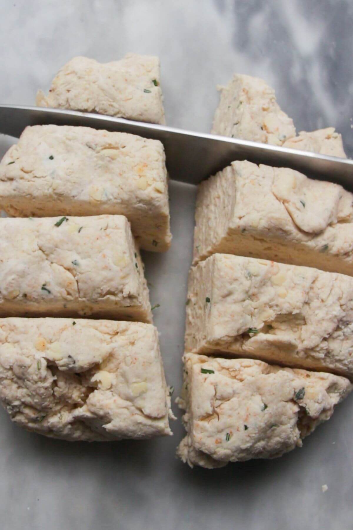 Knife slicing cheese scone dough into 8 pieces.