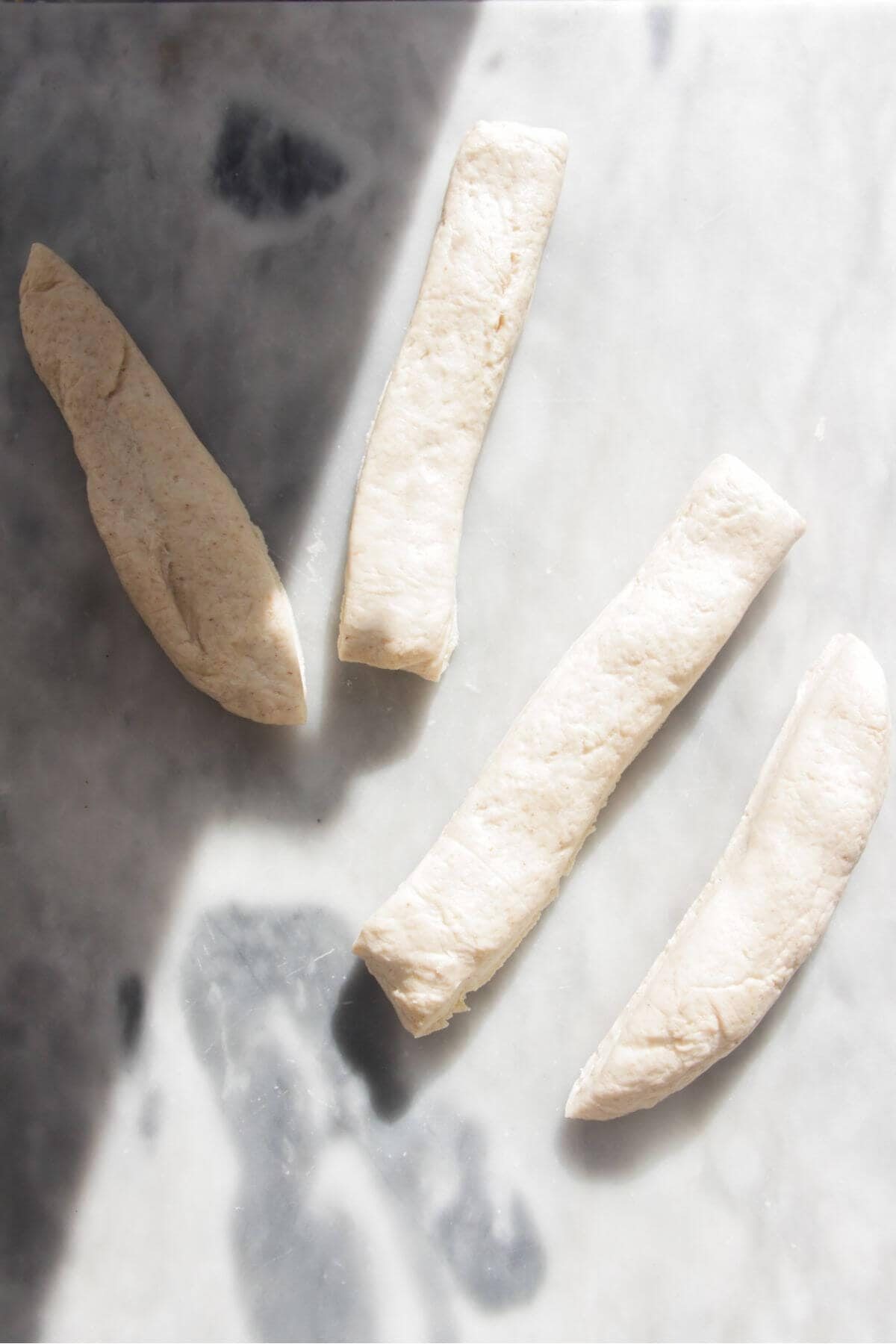 Four long strips of dough on a grey marble background.
