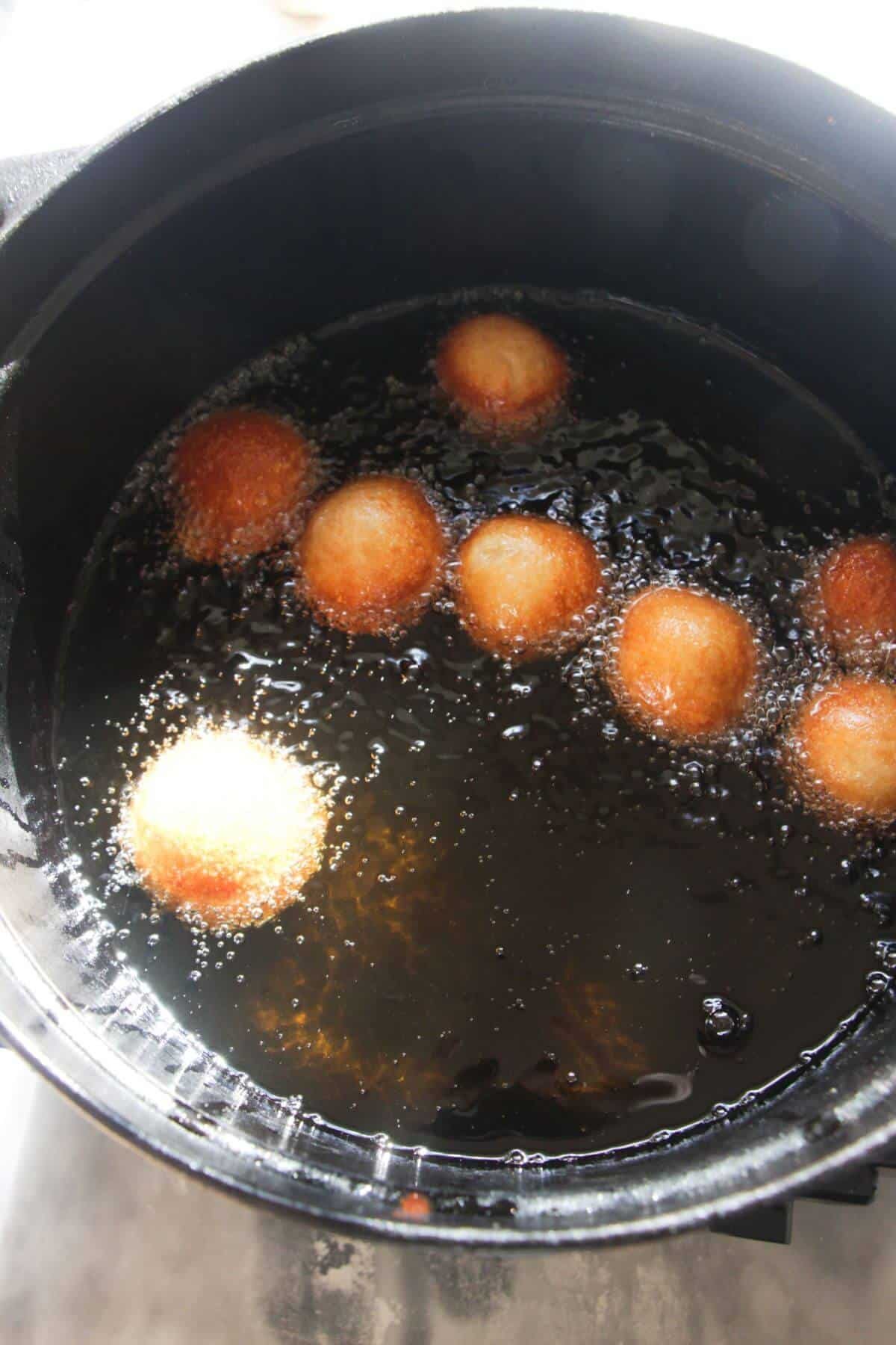 8 donut bites frying in a large black pot of oil.