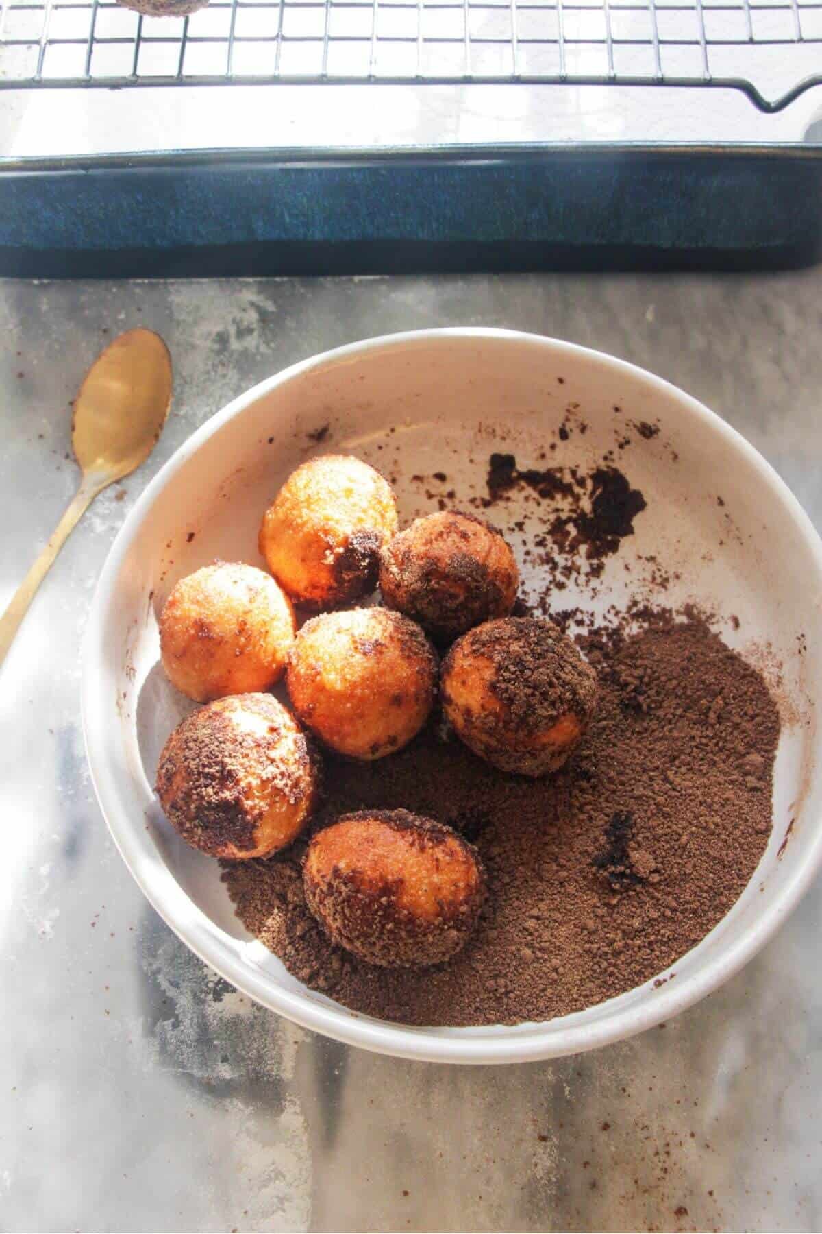 Freshly fried donut bites in a bowl with pumpkin spice sugar, about to be tossed.