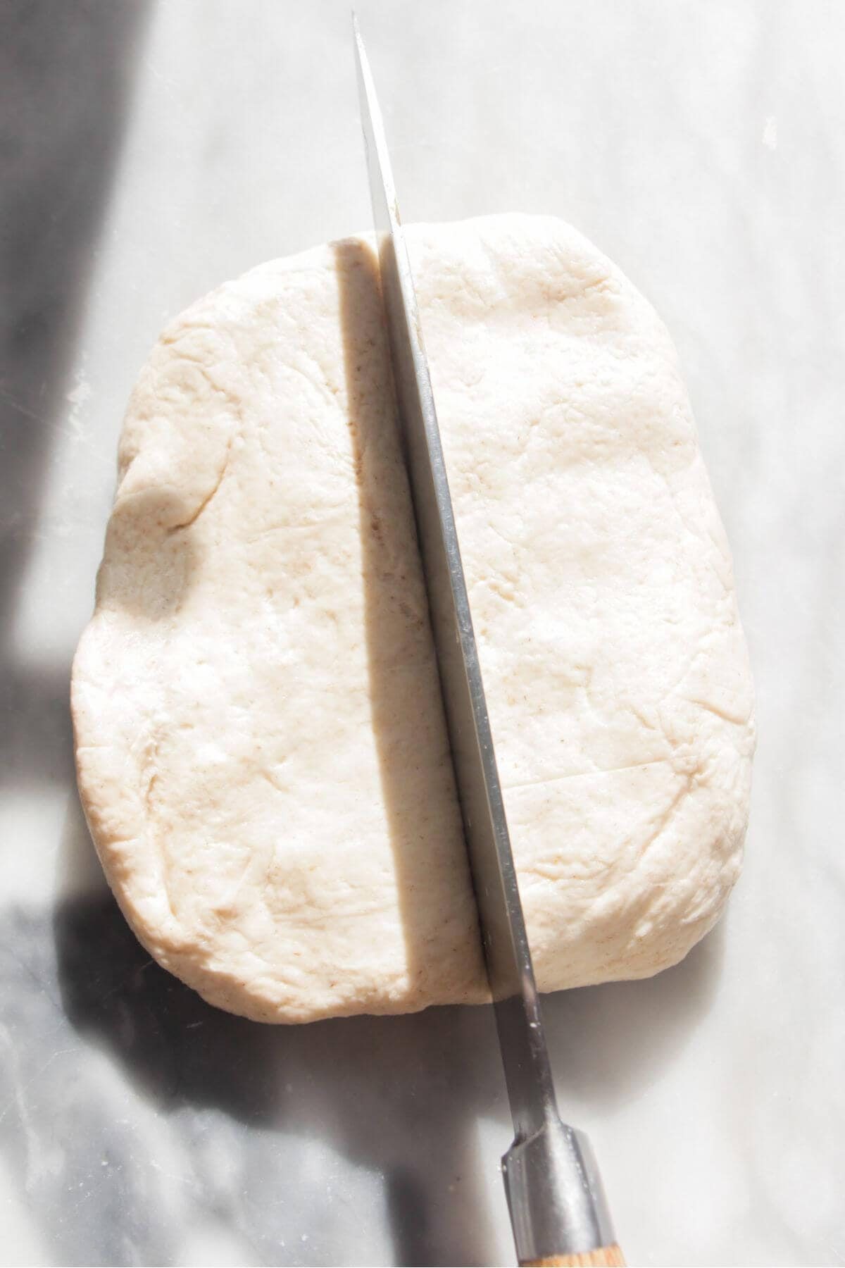 Large knife cutting through a rectangle of dough on a grey marble background.