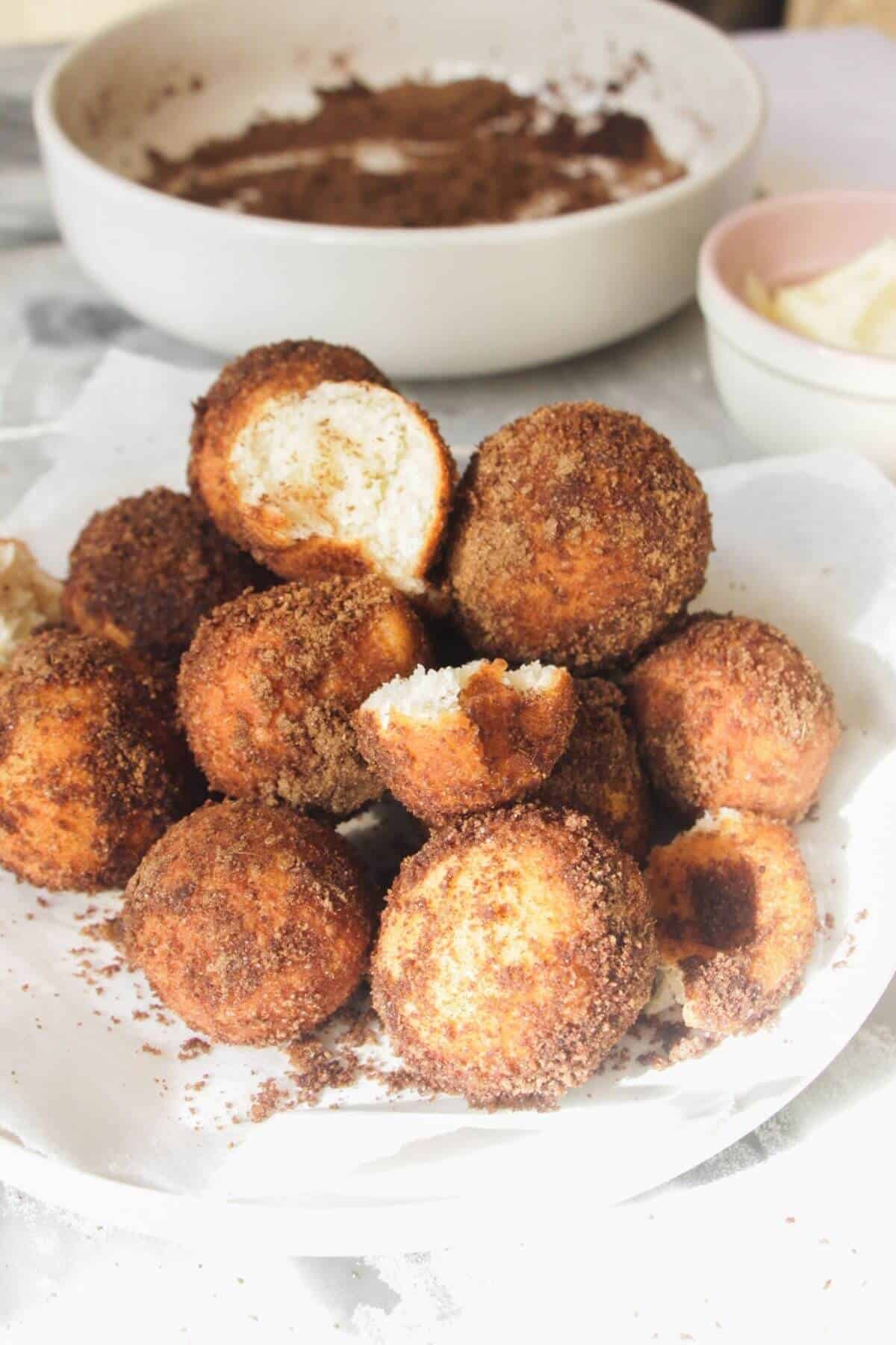 Pile of donut bites on a small white plate with one bite torn open on top.