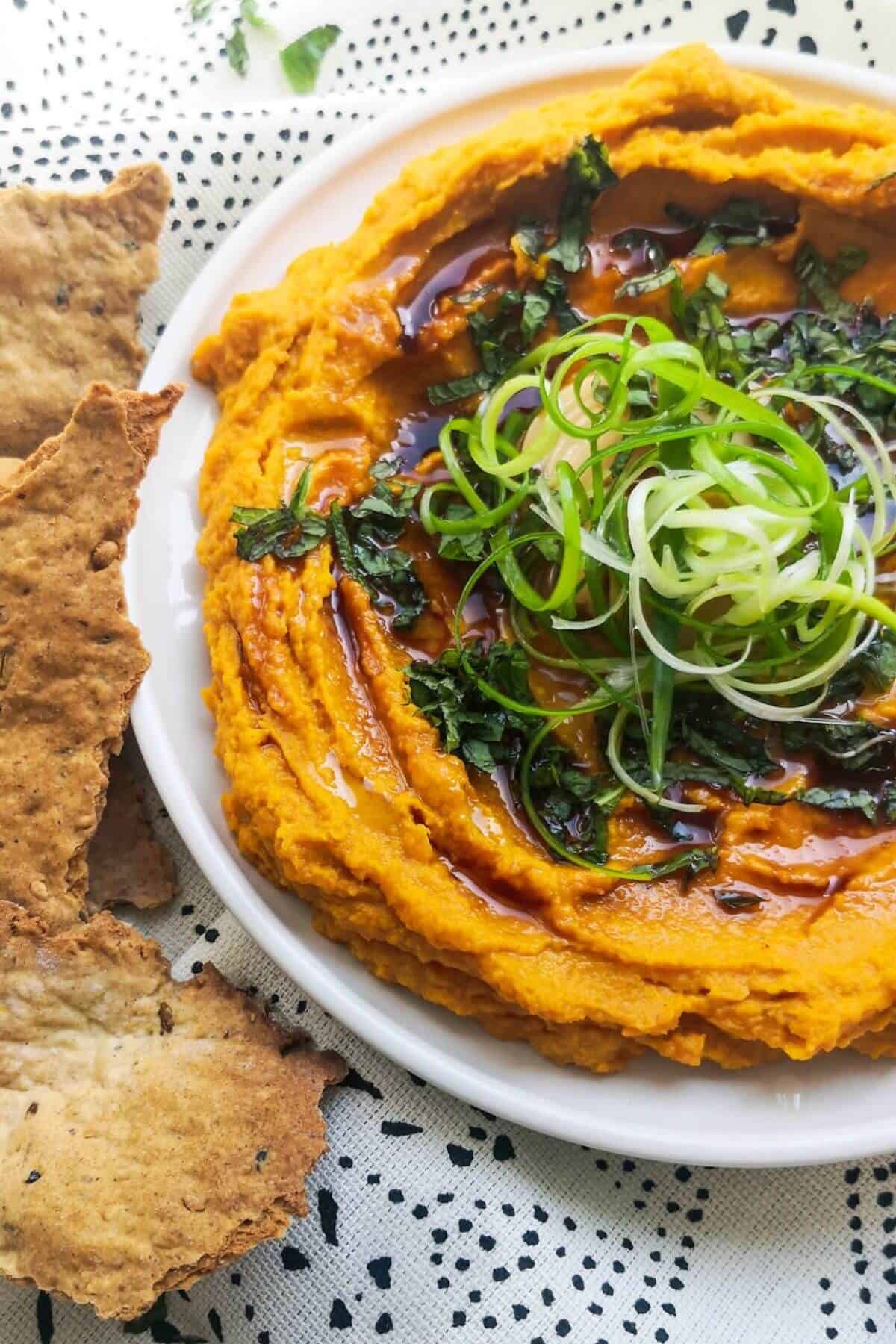 Spiced roasted carrot dip on a white and black patterned background with crackers on the side.
