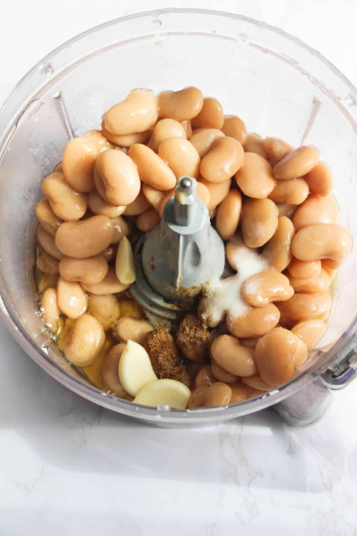 White beans, garlic, salt, lemon juice and olive oil in the bowl of a food processor.