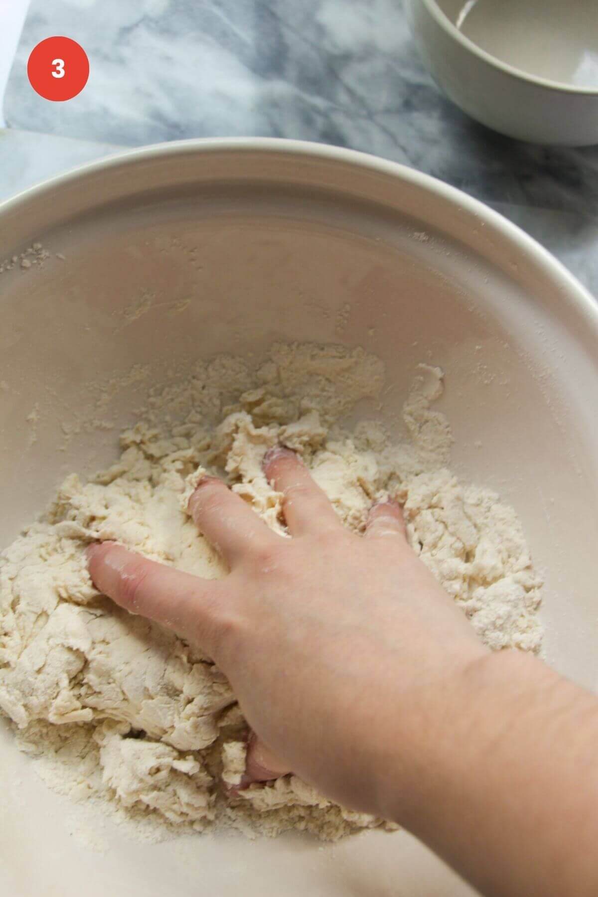 Hand kneading pizza dough in mixing bowl.