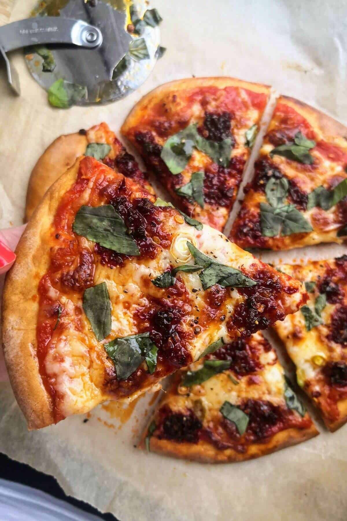 Close up of hand holding a piece of nduja spring onion pizza with pizza slices in the background.