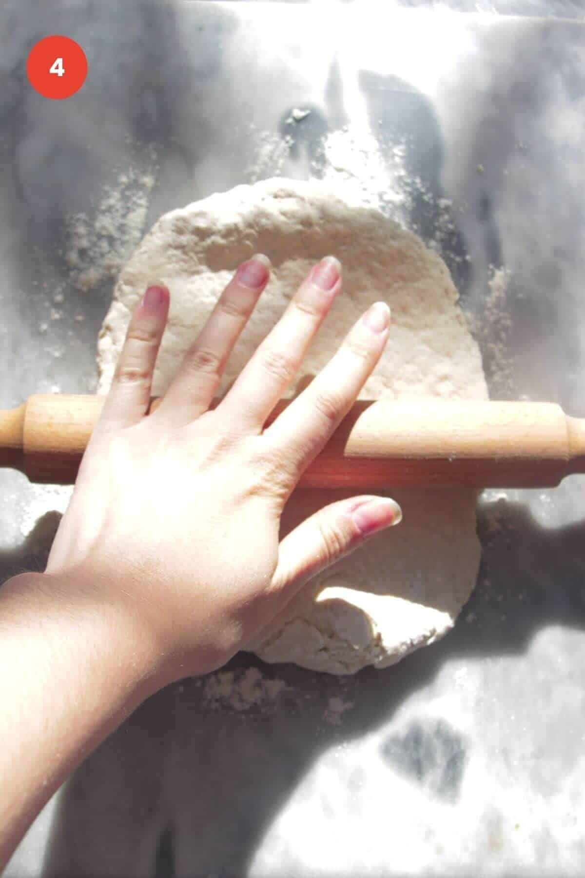 Hand using rolling pin to roll out pizza dough.