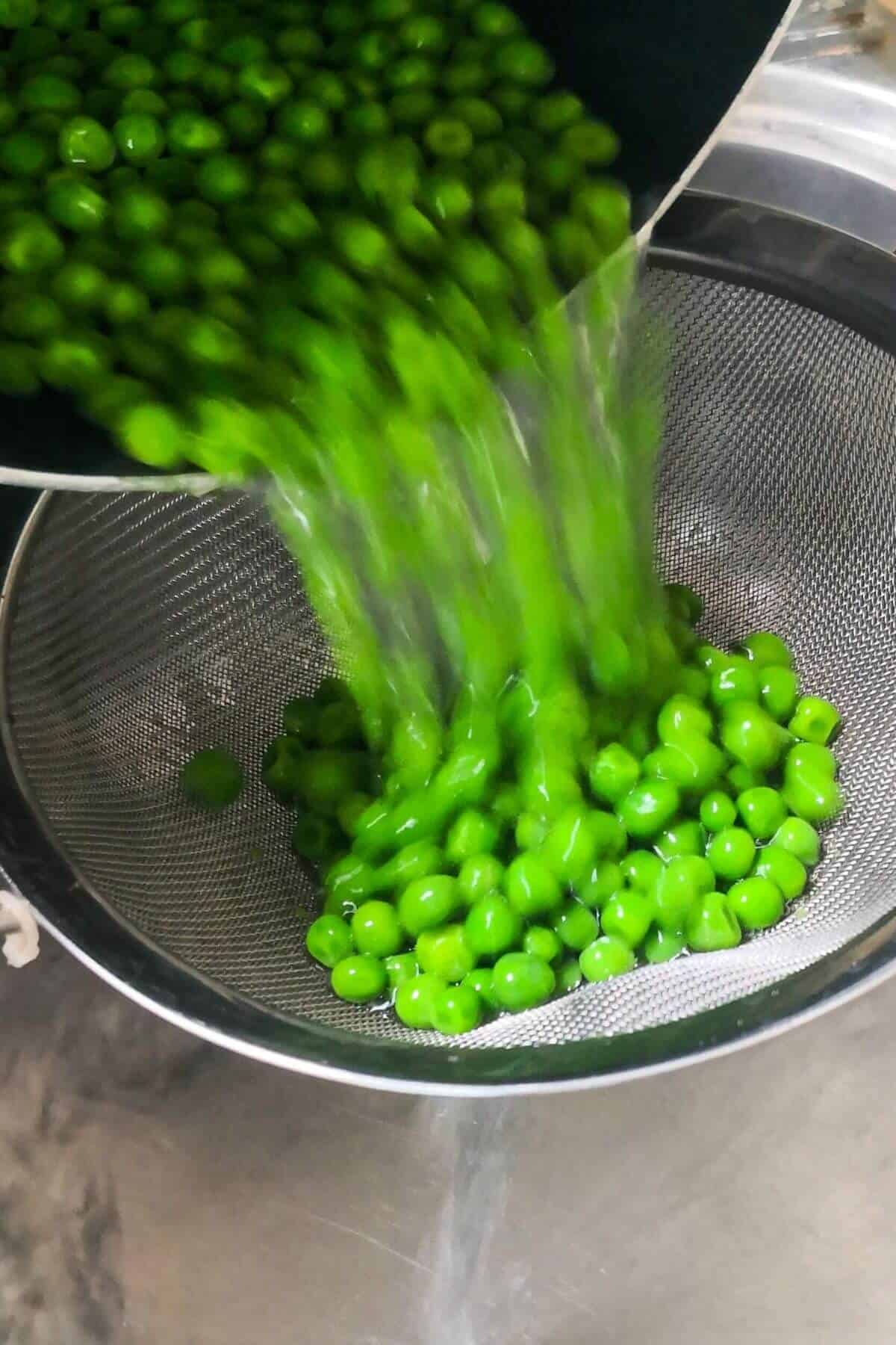 Draining peas from large pot into a silver colander in the sink.