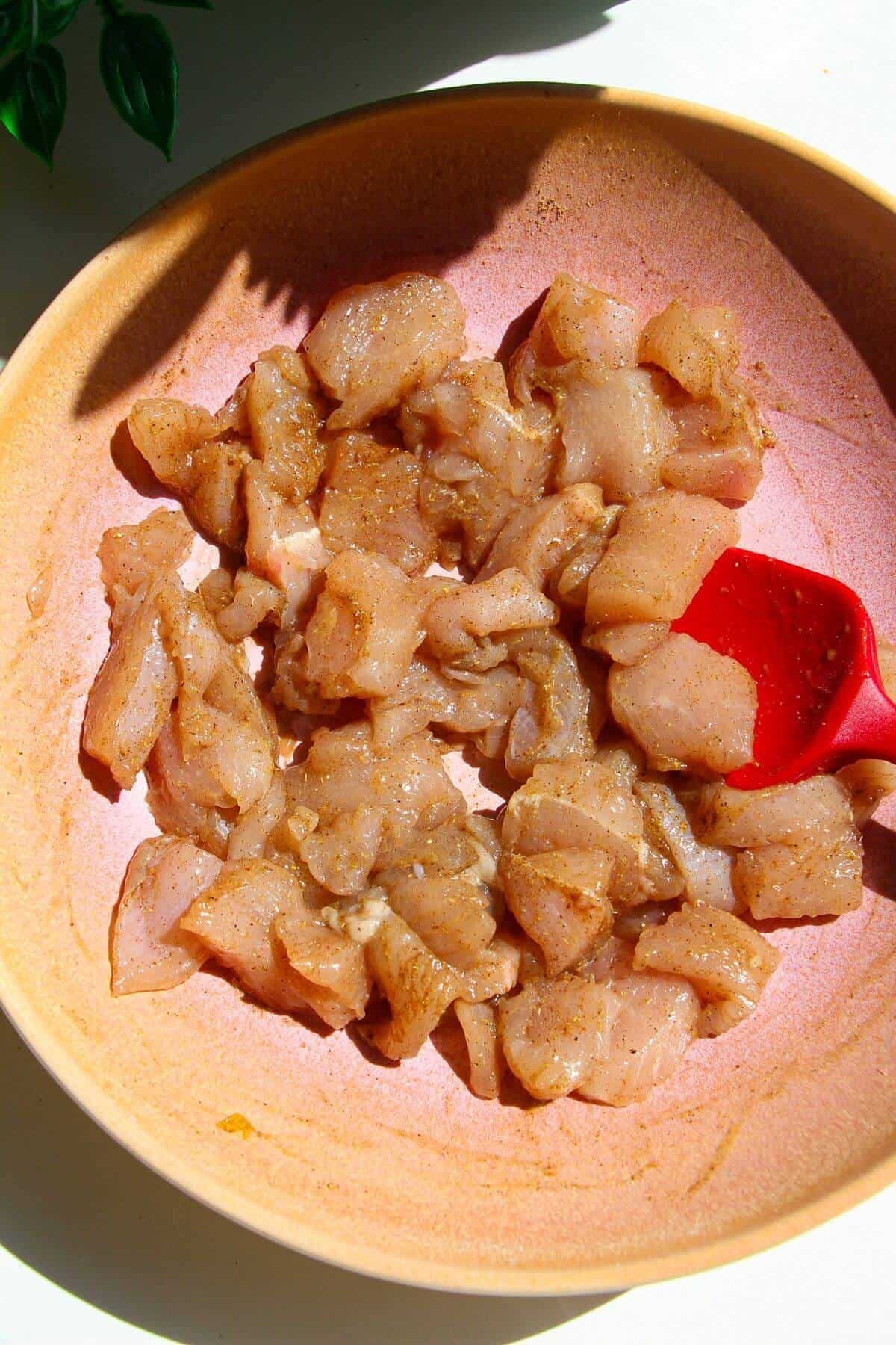 Diced chicken tossed with Chinese five spice and sesame oil in pink bowl.