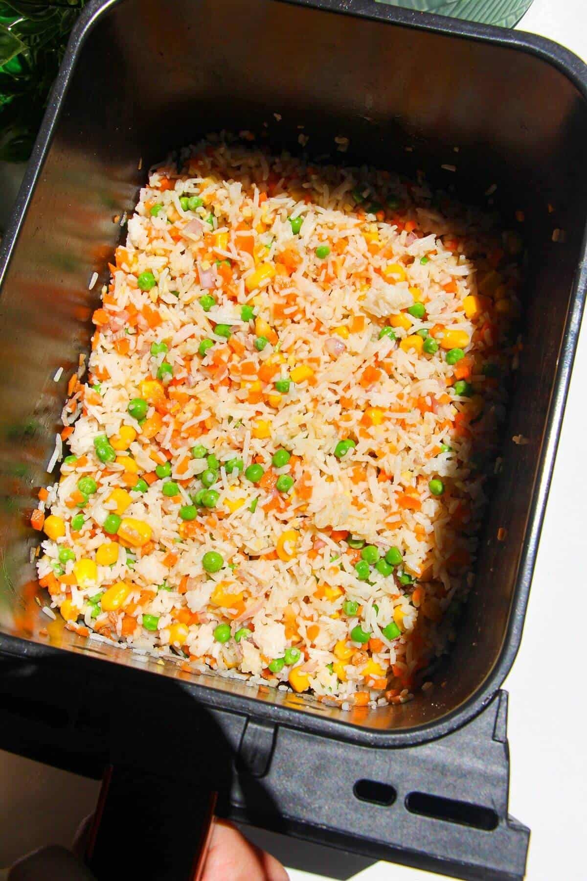 Vegetables and seasoning mixed through rice in air fryer basket.