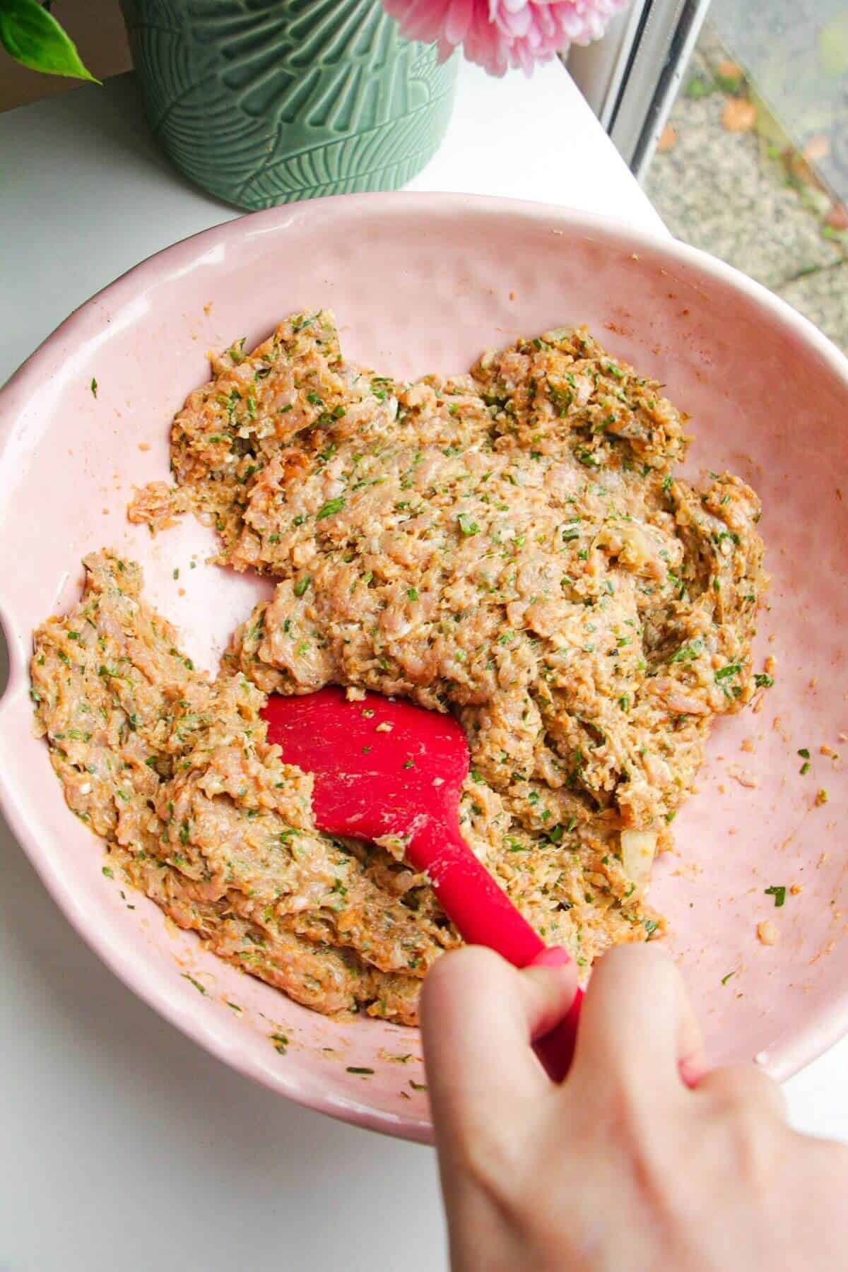 Ground chicken mixed with onion and spices in a large bowl.