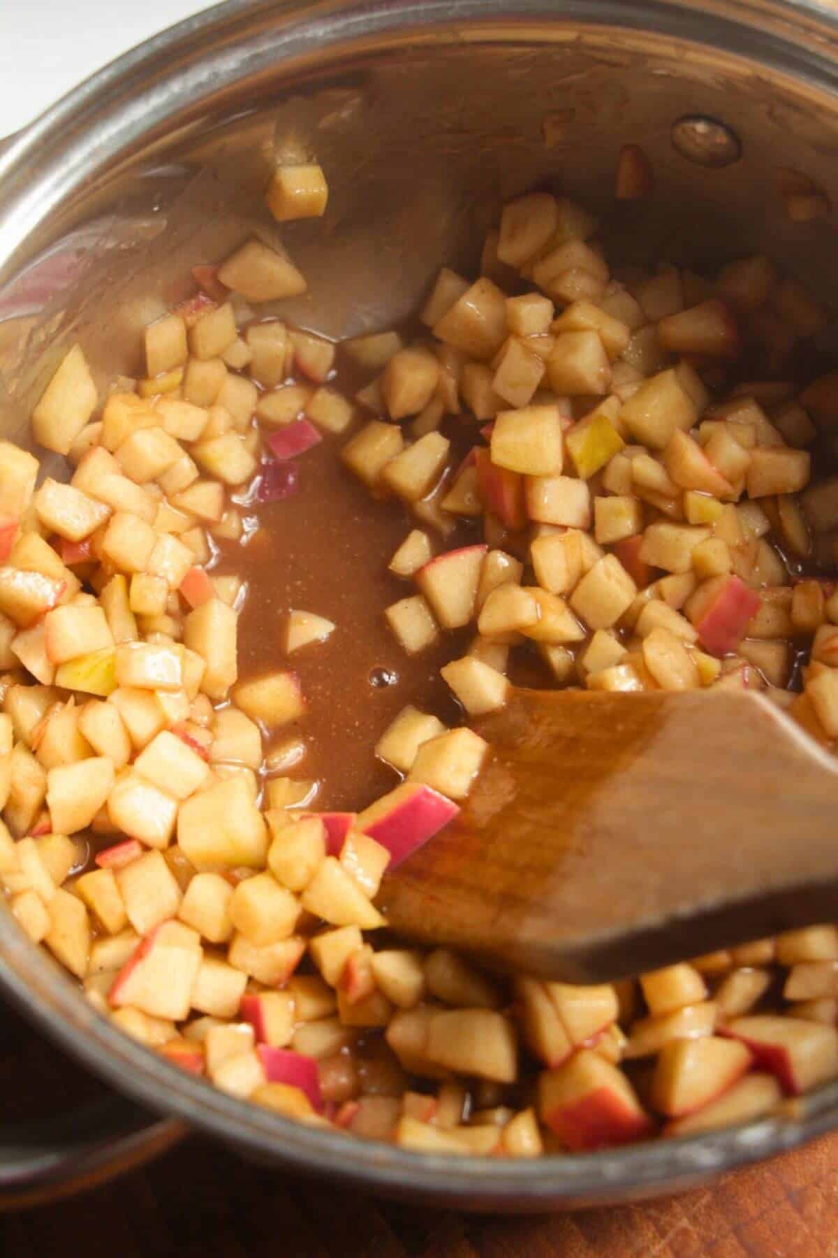 Wooden spatula stirring diced apples in a small pot.