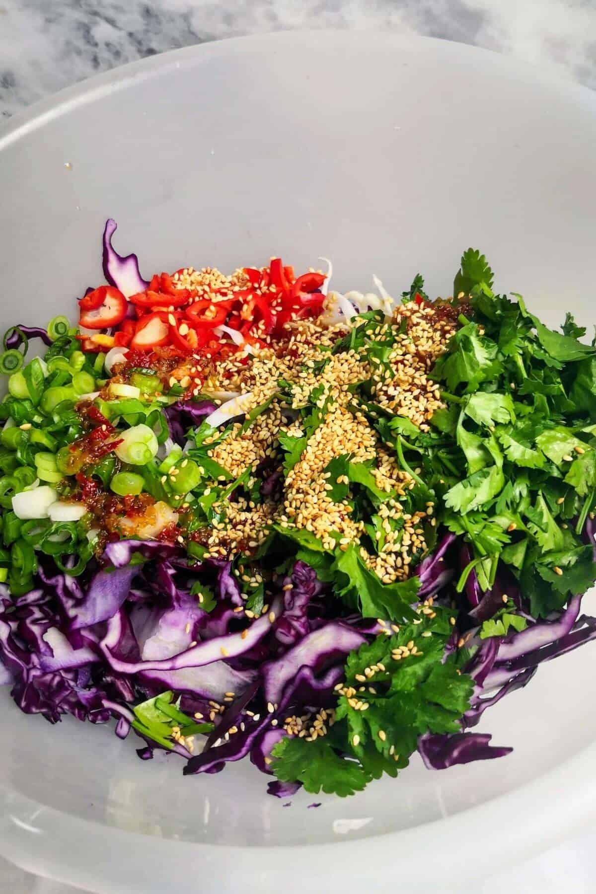 Asian slaw ingredients in a large clear bowl.