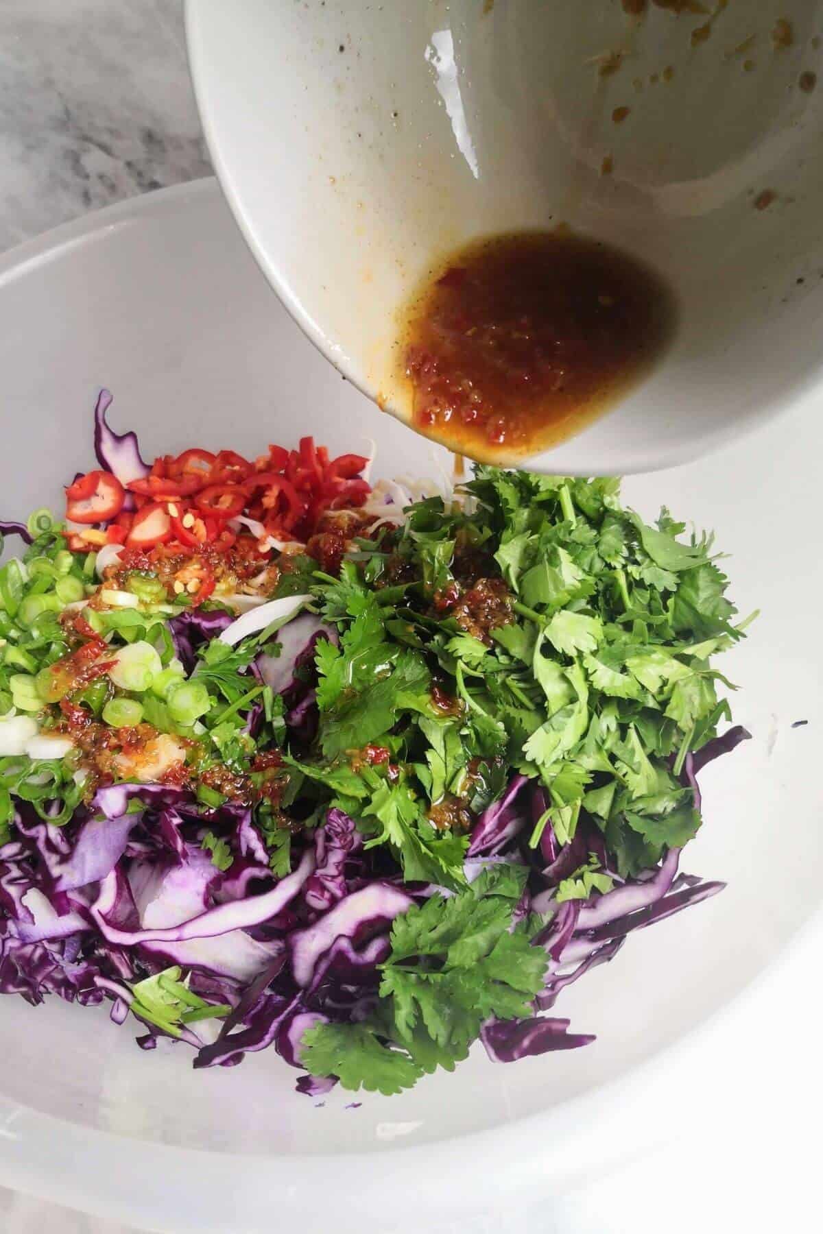 Asian dressing poured into bowl with salad inside.