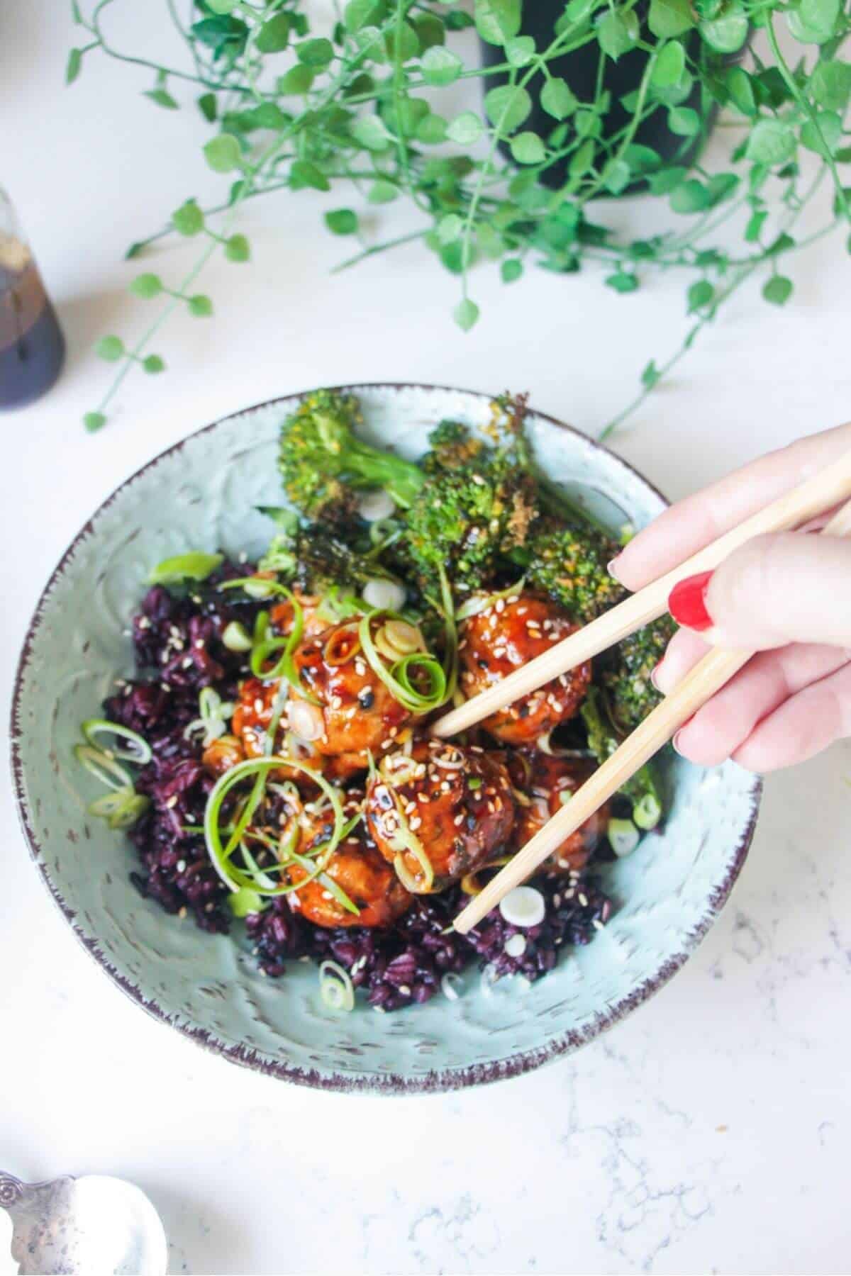 Glazed Asian chicken meatballs with rice and broccoli in a small blue bowl.