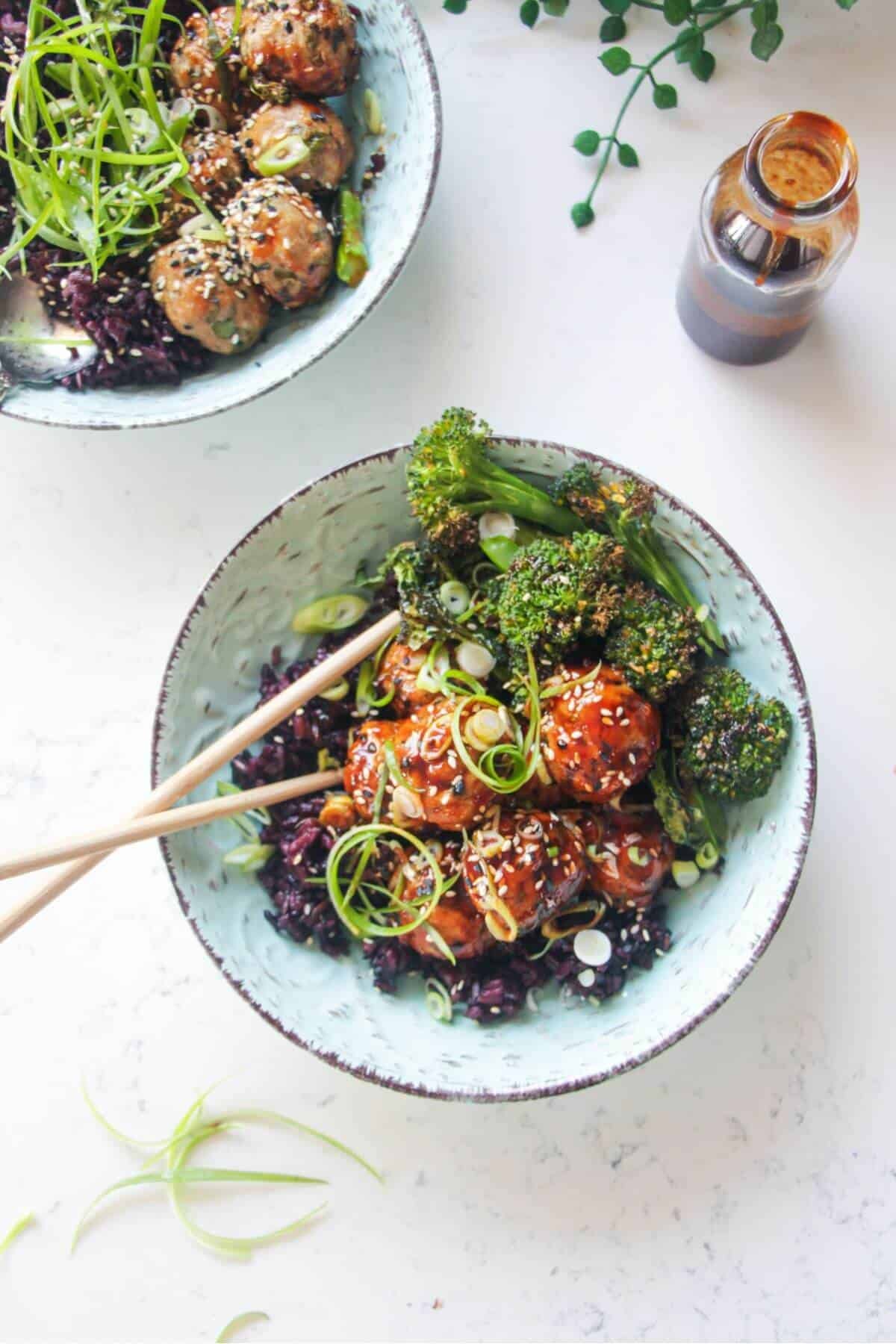 Glazed Asian chicken meatballs with rice and broccoli in a small blue bowl.
